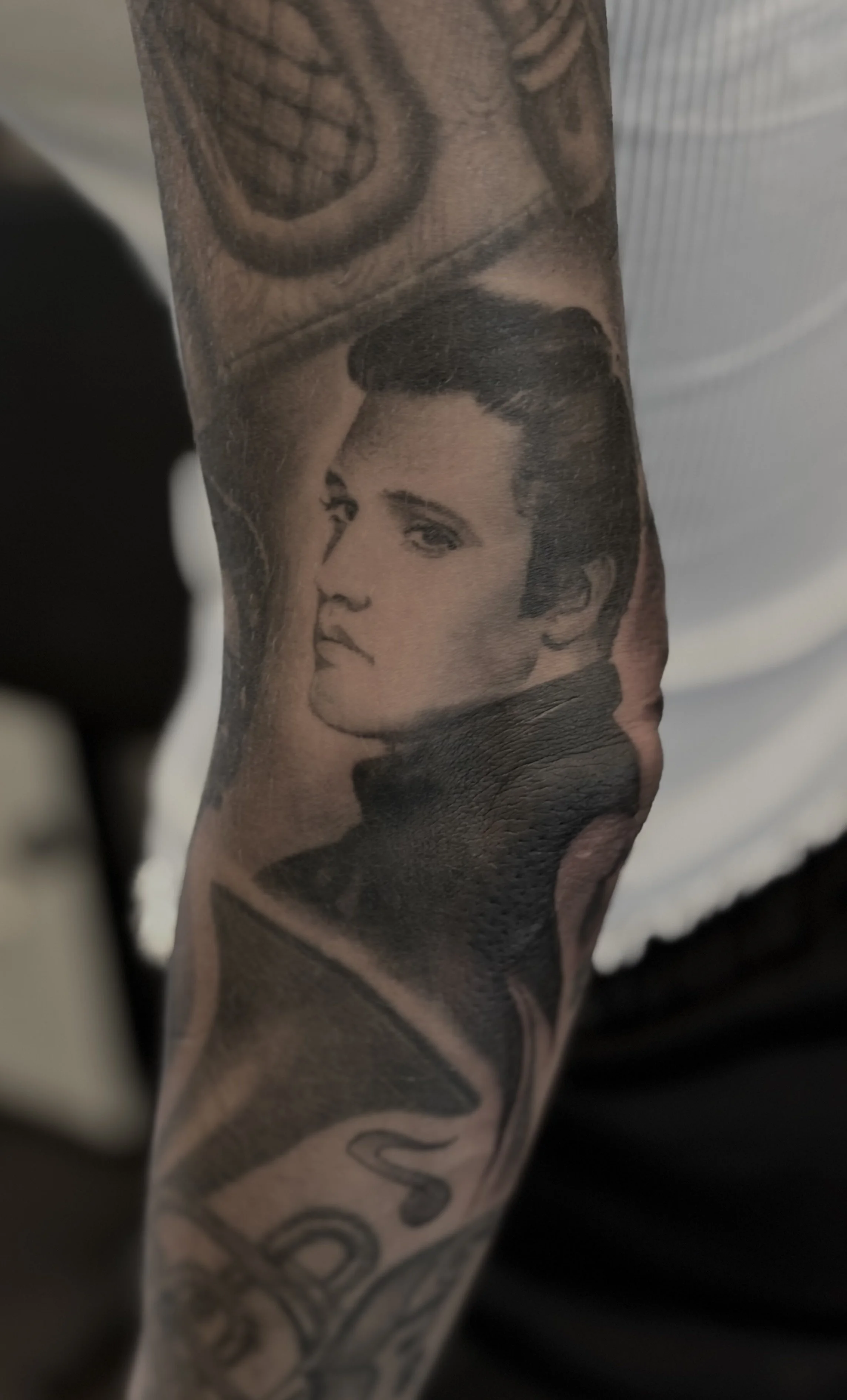 Tattoo of a woman's face with short hair, dark makeup, and a serious expression.