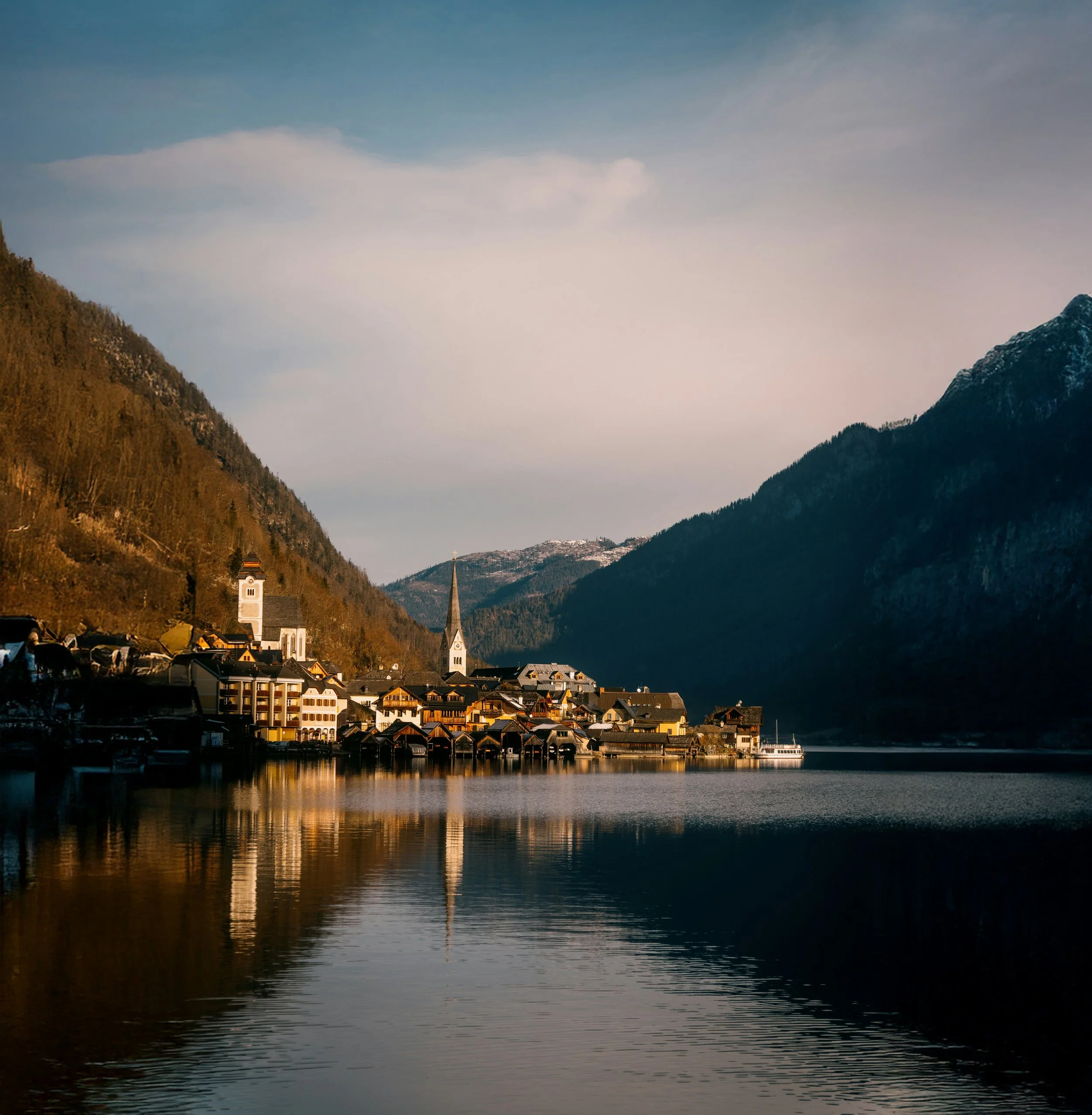 A small village by a lake, surrounded by mountains, with church steeples and reflections in the water.