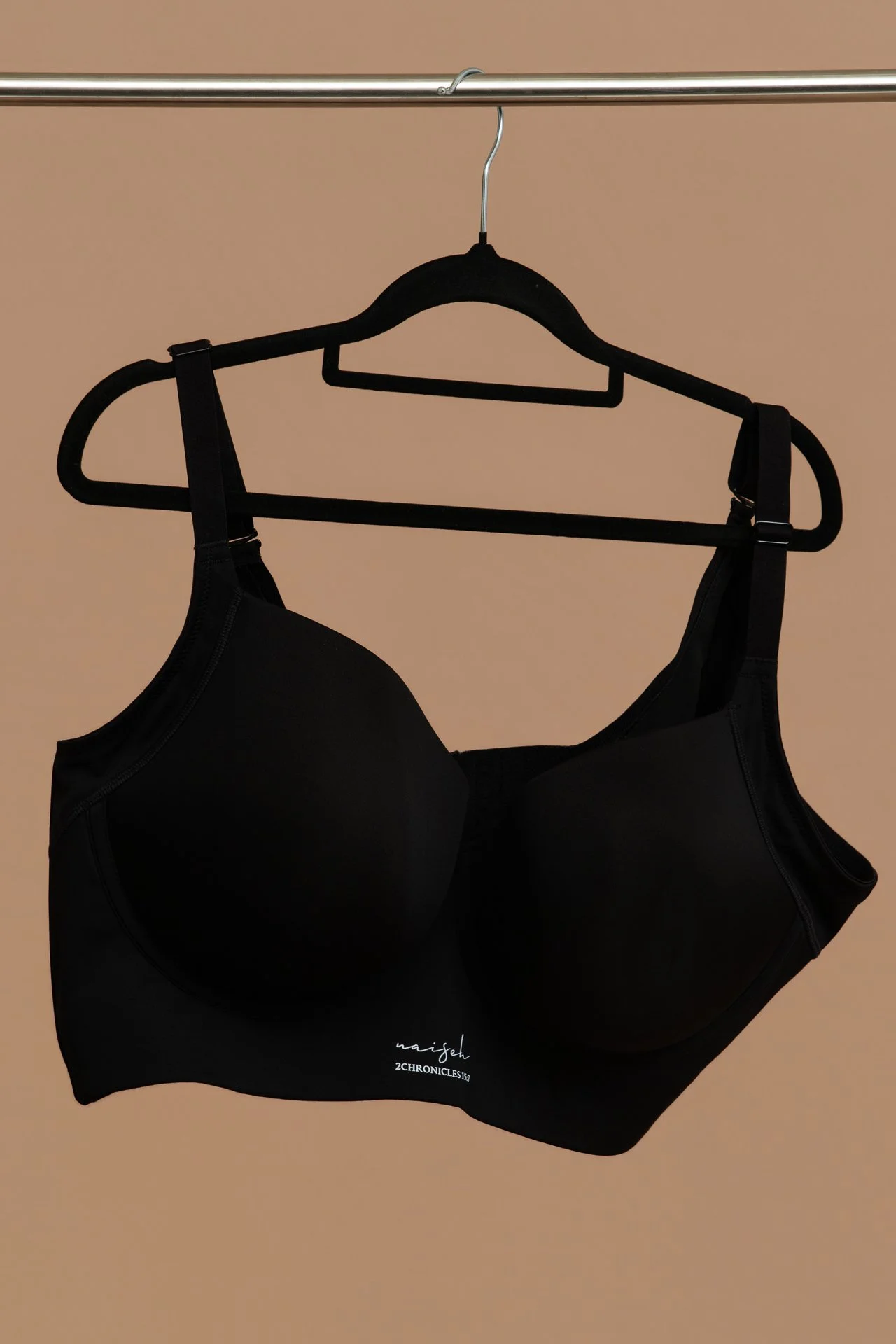 A black bra hanging on a black hanger on a metal clothing rod against a beige background.