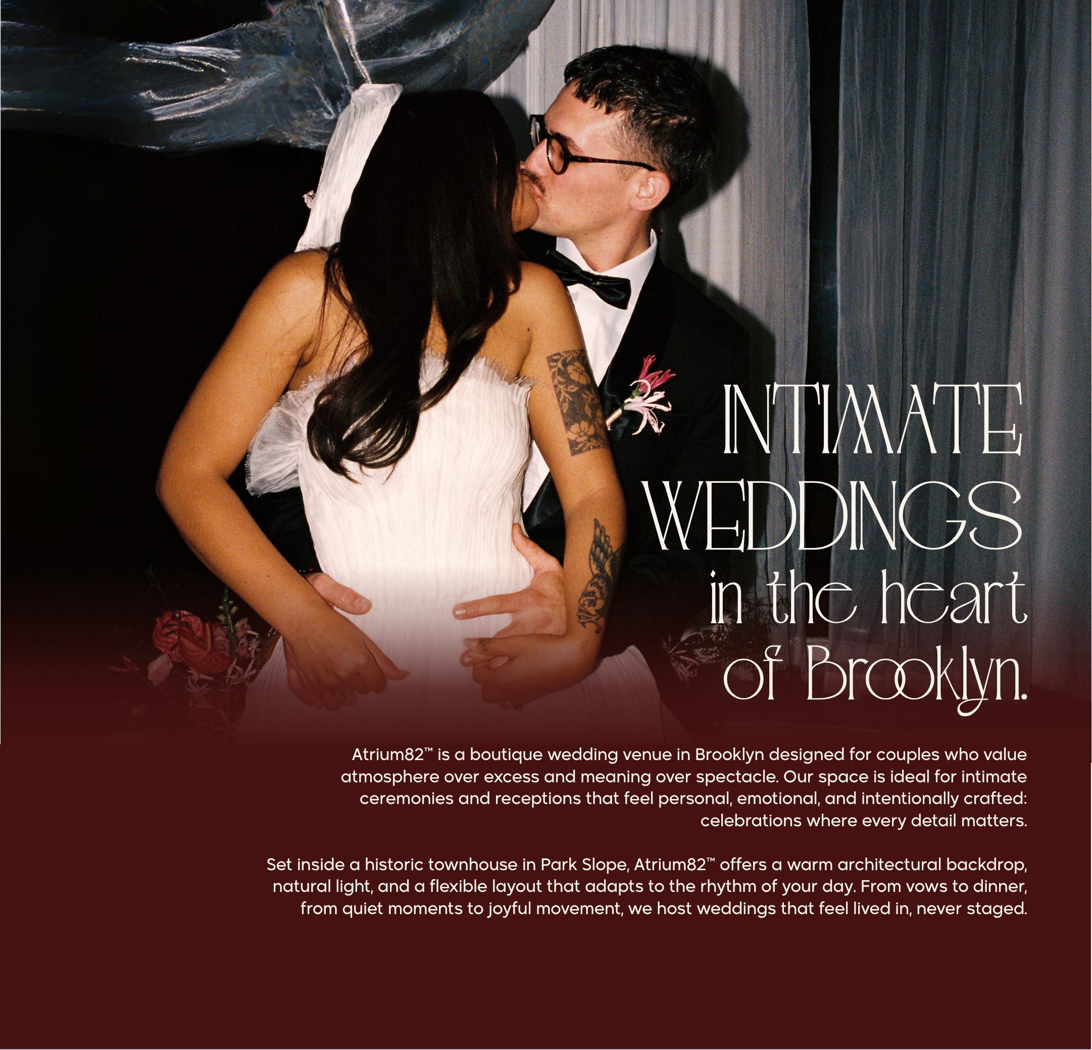 A couple in wedding attire sharing a kiss, with a woman in a white gown and a man in a black tuxedo, in front of a dark background with curtains and plastic draping.