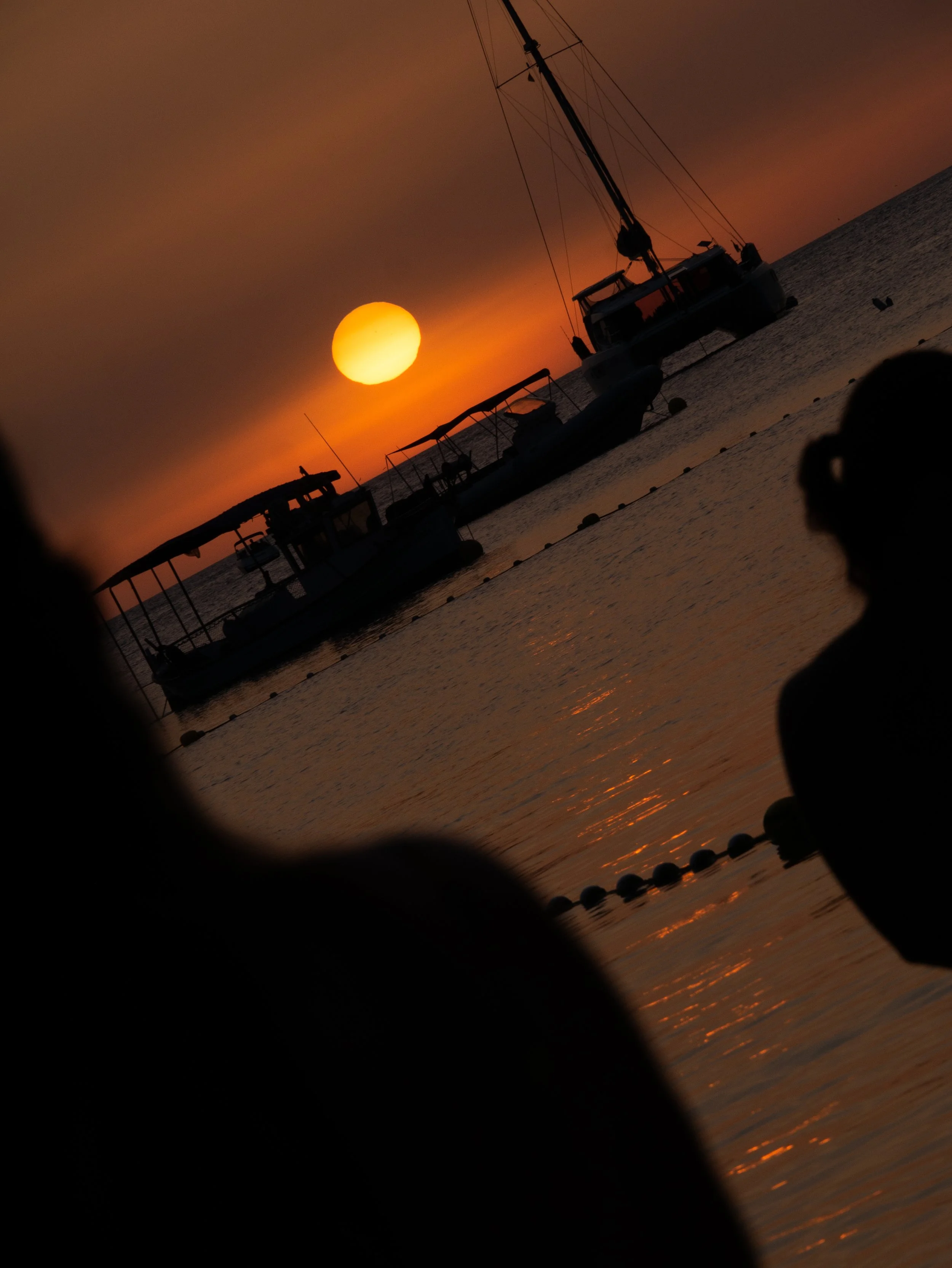 Sunset over water with boats, seen through a porthole with dark edges in the foreground.