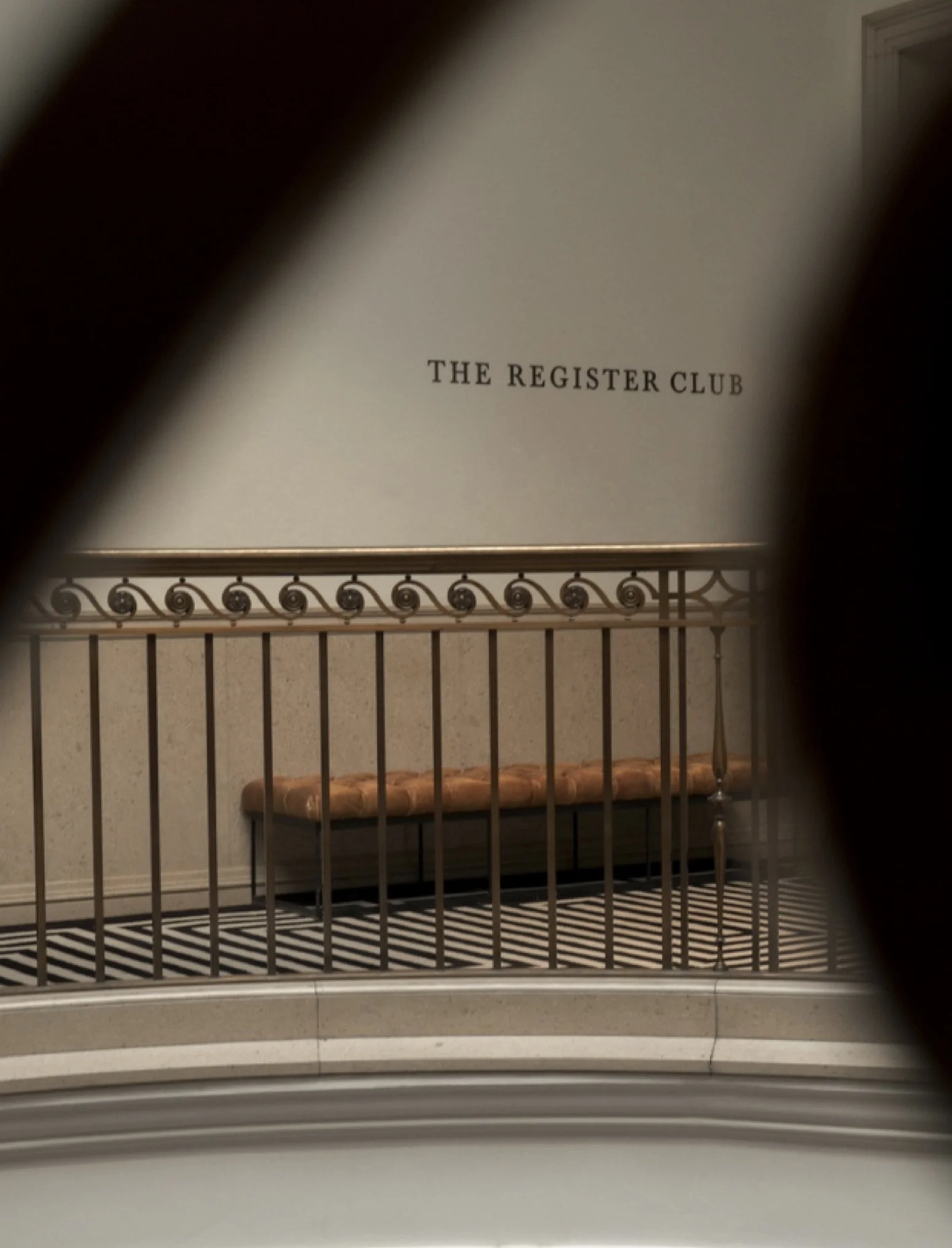 Interior view of a building with a staircase, a bench with a cushioned seat, and a white wall with the text 'The Register Club' visible.