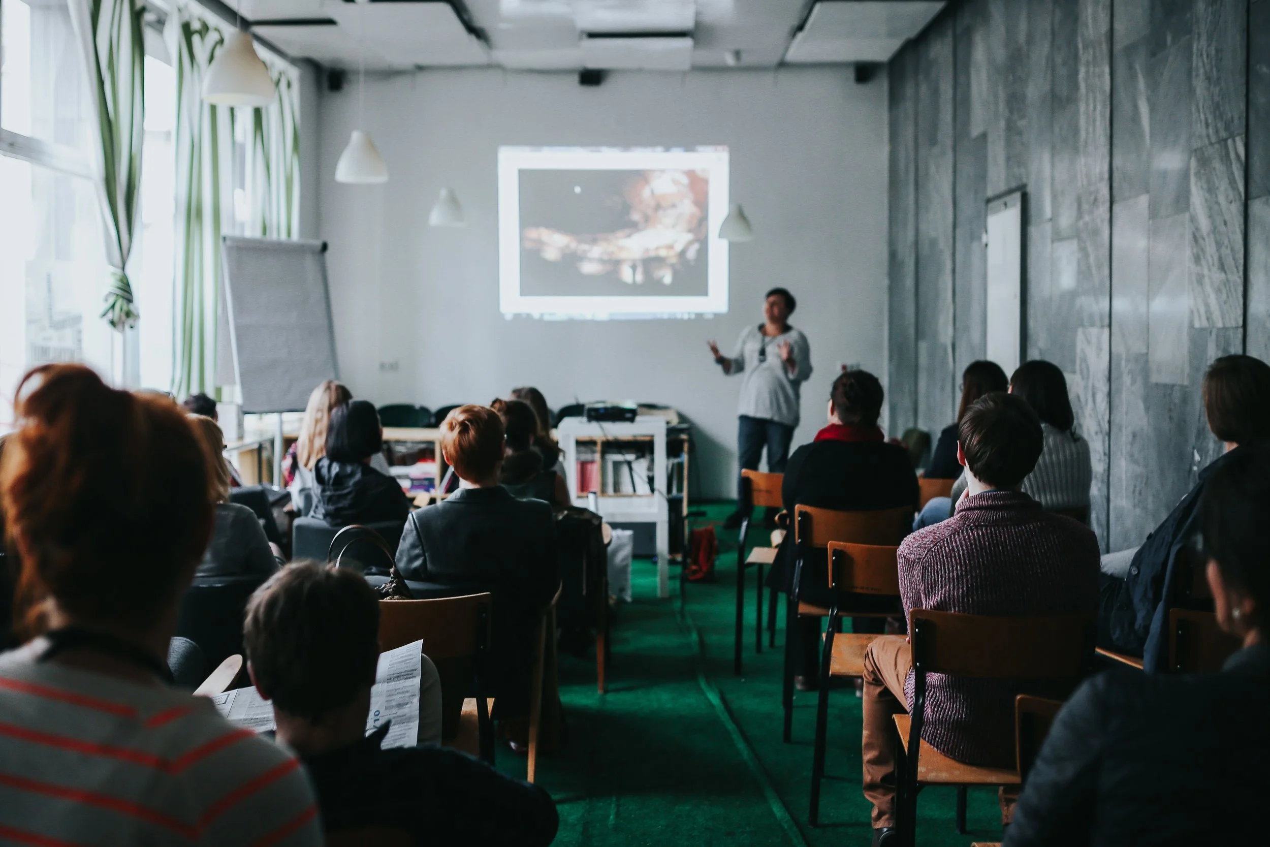 A woman giving a presentation to a group of people in a conference room with a projected slide on the wall.
