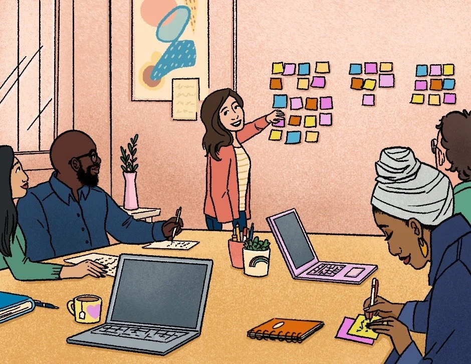 A diverse group of people in a meeting room, with sticky notes on the wall, a woman presenting, and laptops and notebooks on the table.