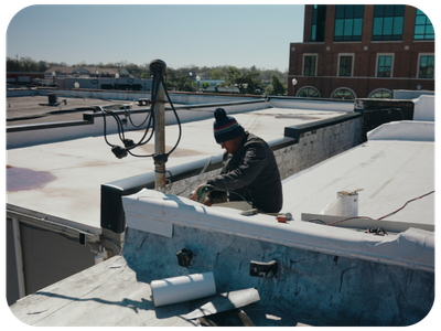 A person working on a rooftop with various tools and equipment, wearing a beanie and jacket, with a cityscape in the background.
