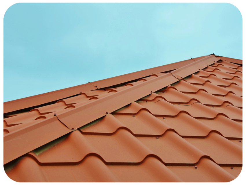 Close-up of a red clay tile roof with a metal ridge cap under a clear, blue sky.