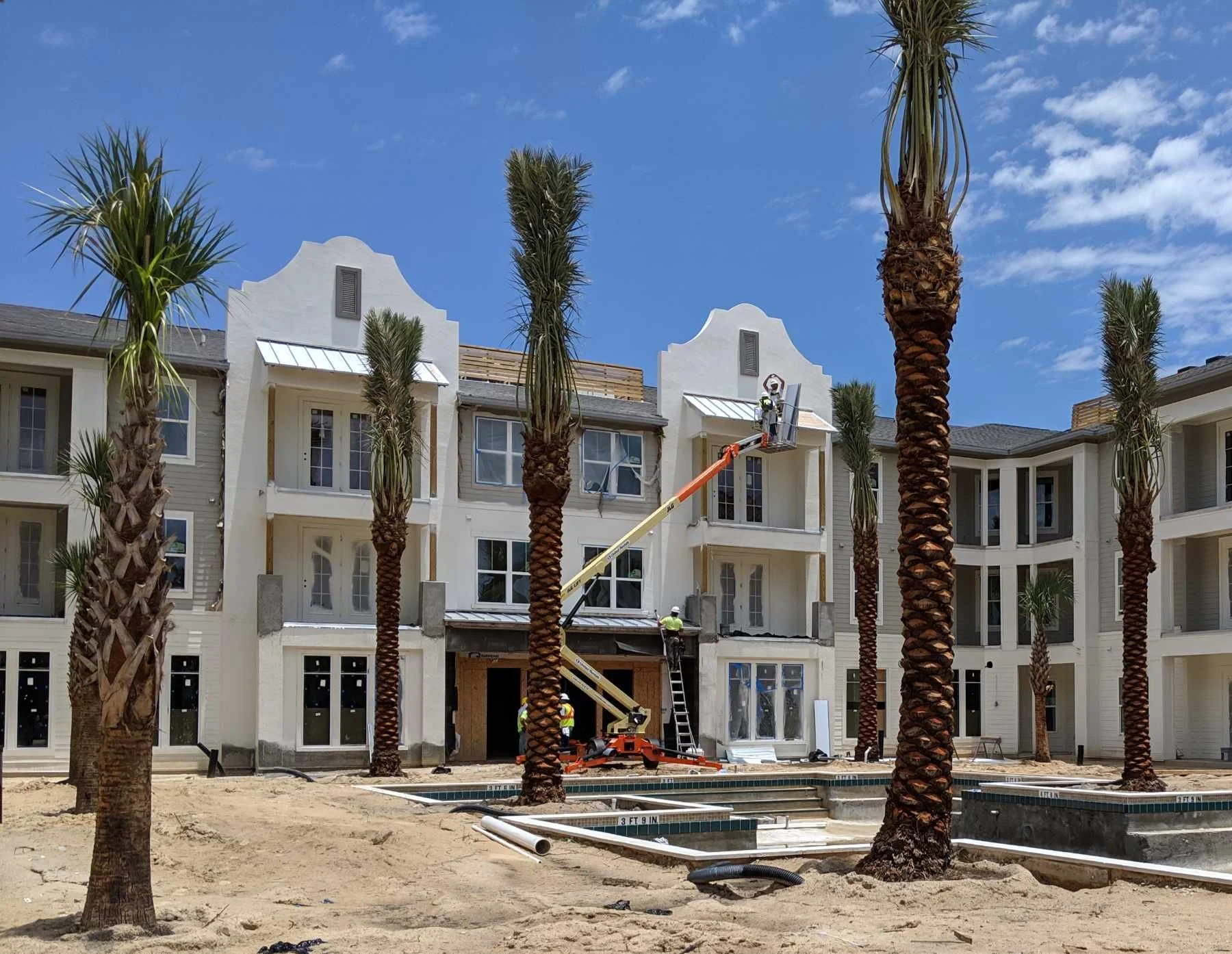 Construction workers installing windows on a multi-story building with tall palm trees and blue sky in the background.
