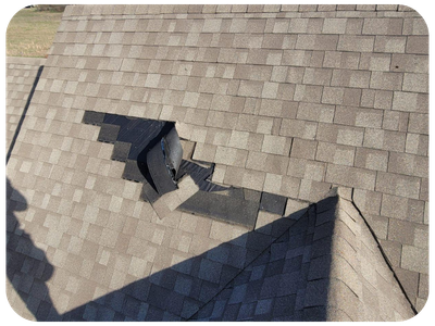 A large section of shingles on a roof has a hole or damage, with shingles displaced around it.
