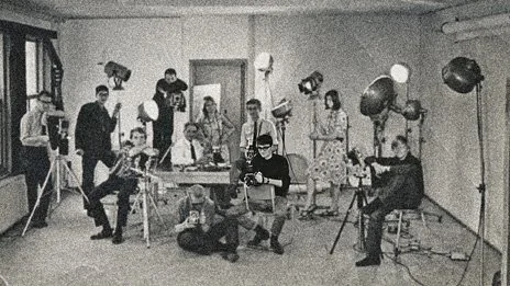 Groupe de personnes avec des appareils photo et des lumières en studio de photographie en noir et blanc.