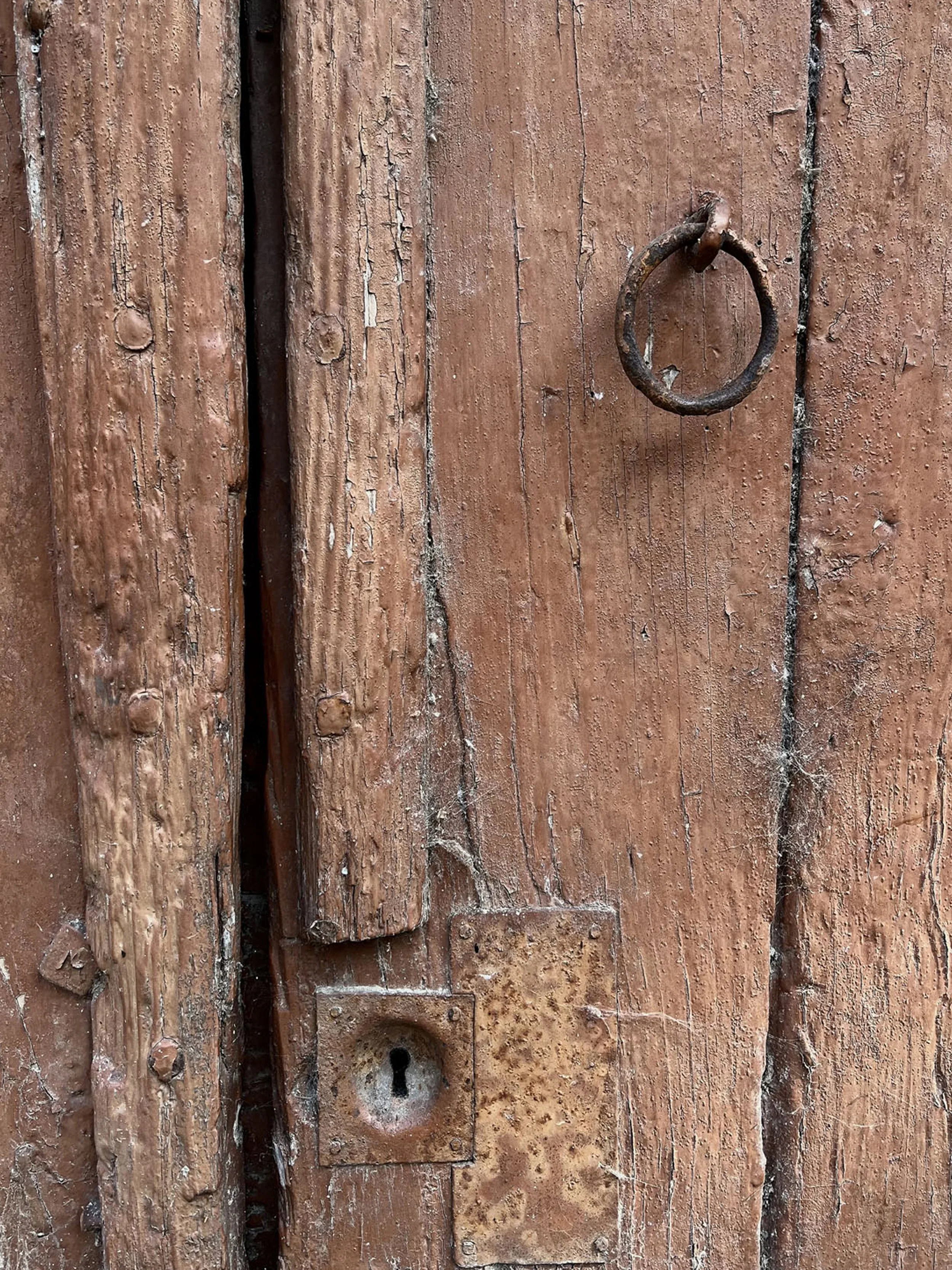 Vieille porte en bois rouge avec poignée en fer patiné.