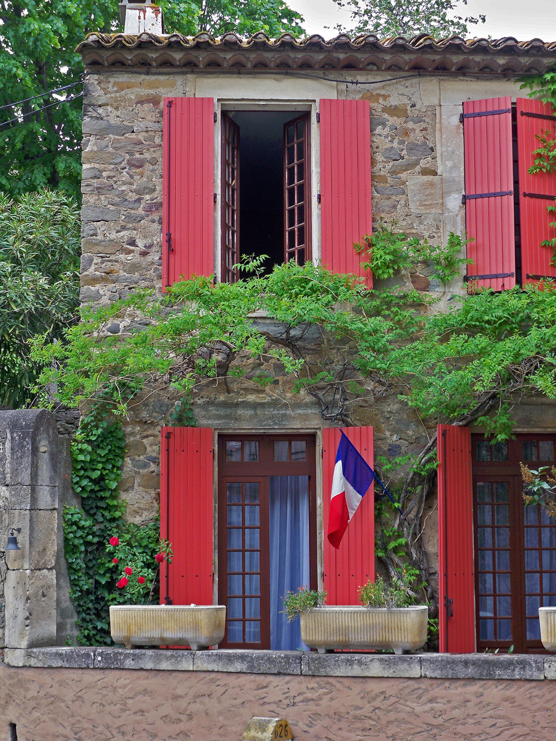 Une maison en pierre avec des volets rouges…