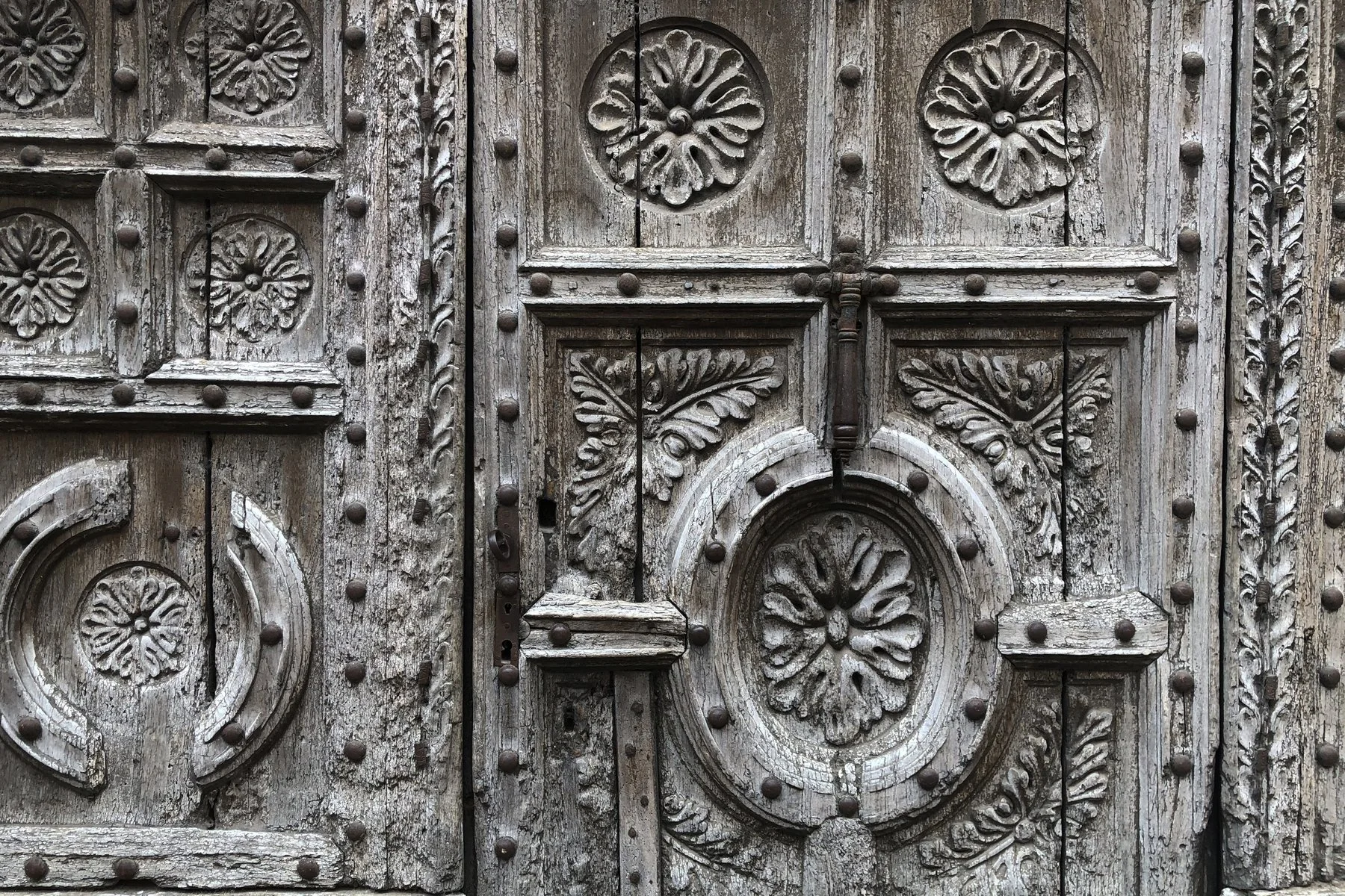 Porte ancienne en bois sculpté avec motifs floraux et clous de fer.