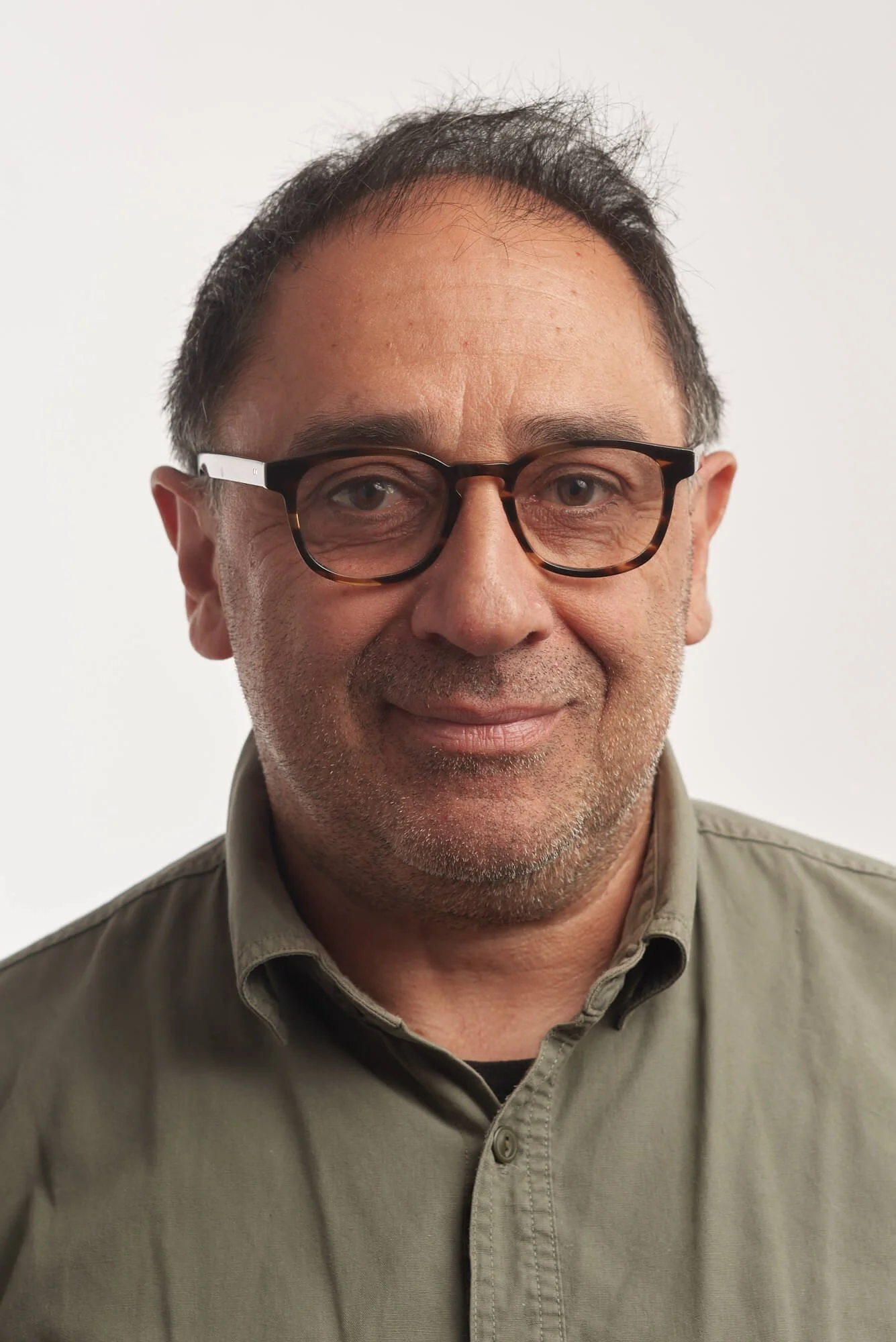 Portrait d'un homme portant des lunettes, souriant légèrement, habillé d'une chemise beige, fond blanc