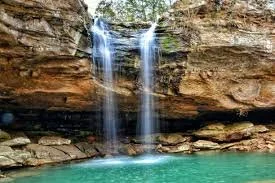A double waterfall cascading into a turquoise pool surrounded by rocky cliffs.