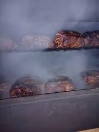 Meat cooking on a grill with smoke rising.