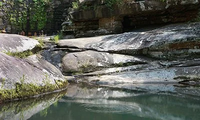 A small waterfall flowing over layered rocks into a calm pool surrounded by greenery.