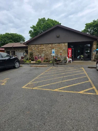 A small building with a stone facade and a dark brown roof, parking spaces in front, some cars parked, and a Coca-Cola vending machine outside.