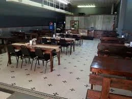 Empty restaurant dining area with wooden tables and chairs, tiled floor, and industrial-style ceiling.