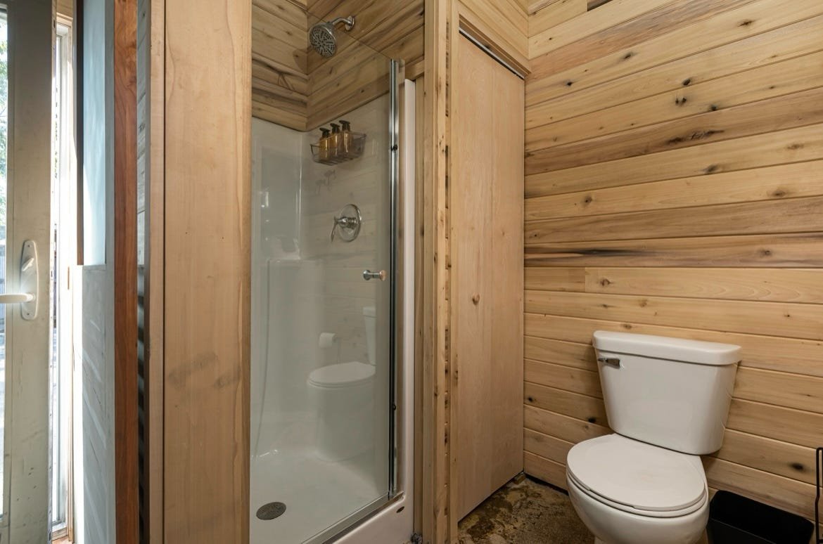Wood-paneled bathroom with a toilet and a glass-enclosed shower stall.