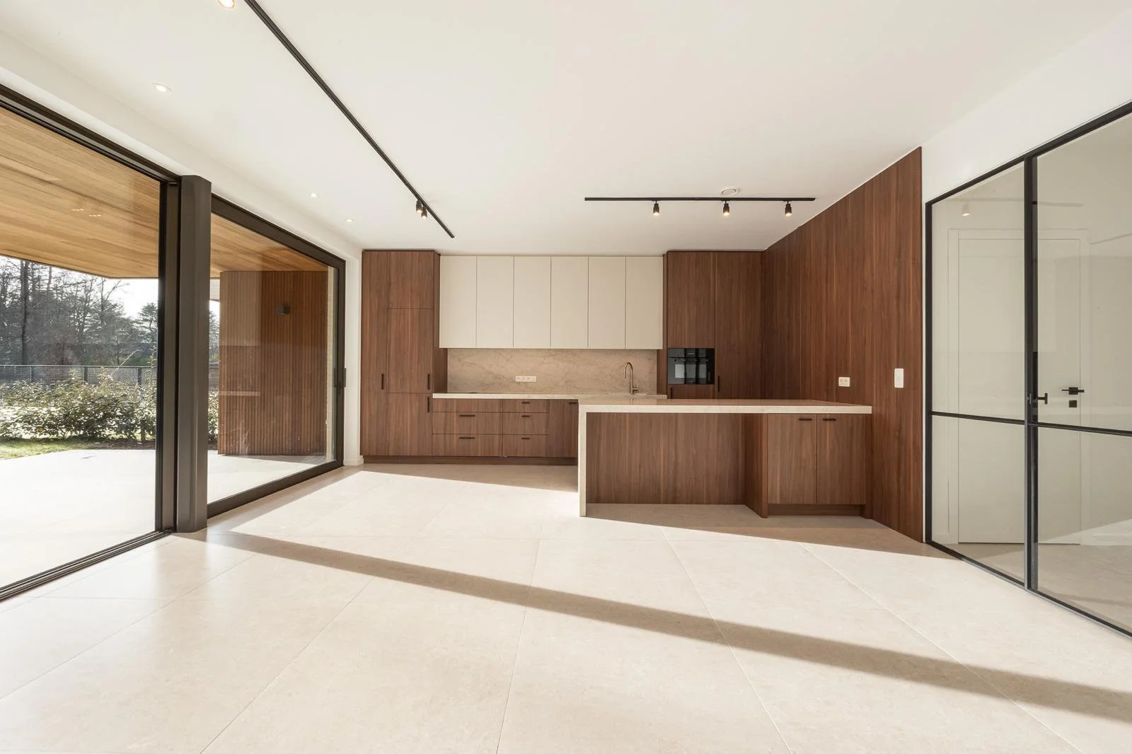 Modern kitchen with wooden cabinetry, white upper cabinets, marble backsplash, and large sliding glass doors leading outside.