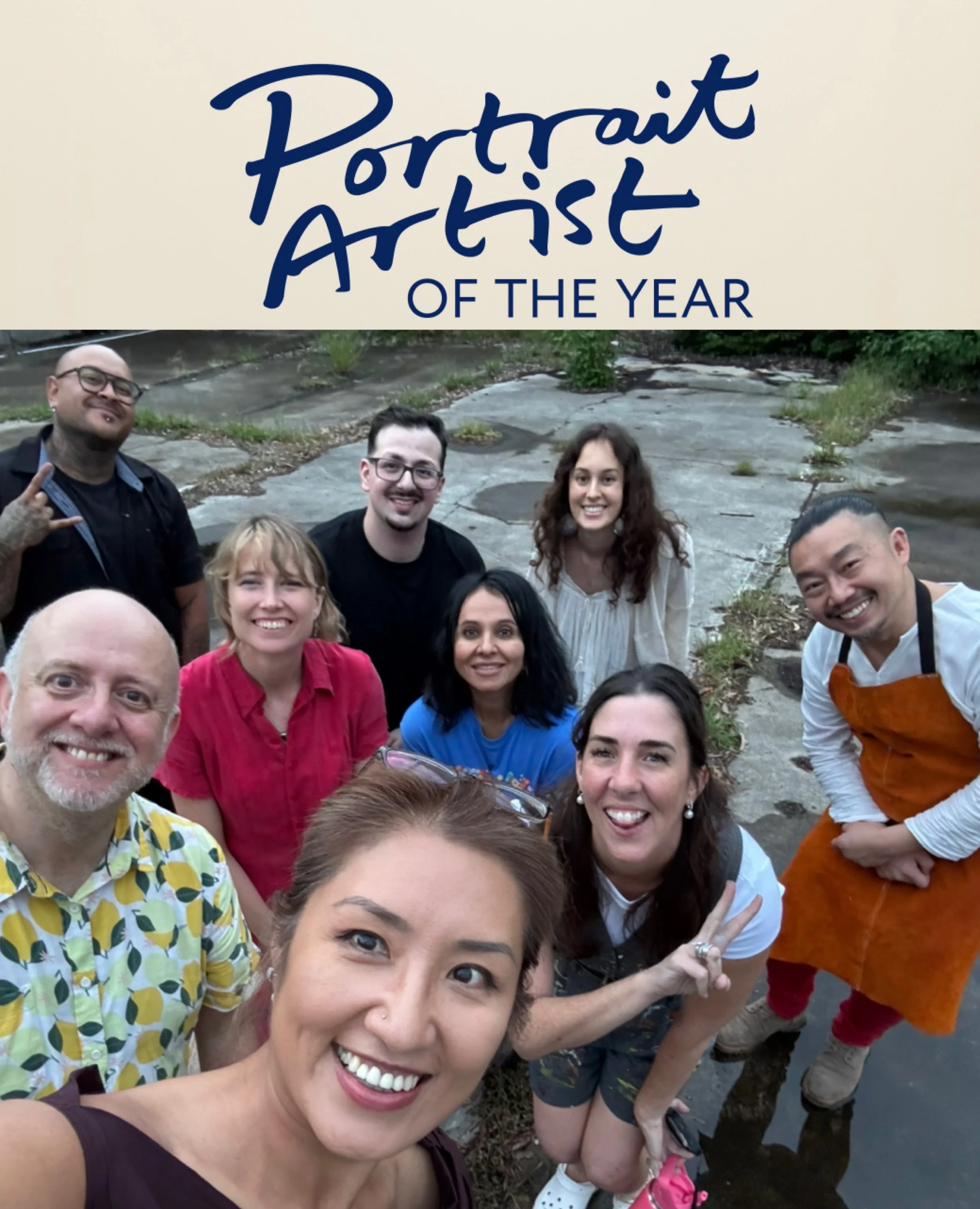 A group of smiling people taking a selfie outdoors near a creek, with some people making peace signs.