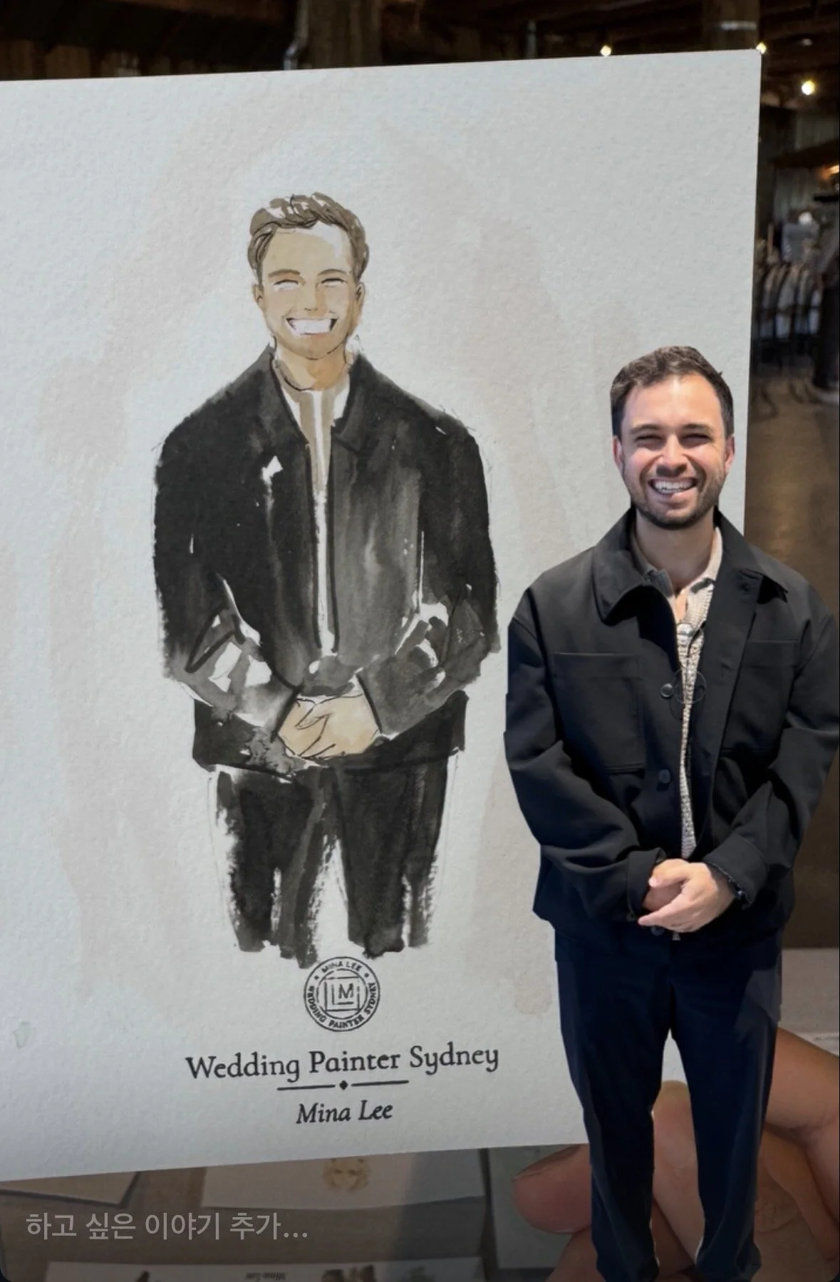 A person standing next to a sign with a watercolor portrait of a smiling man in a black jacket. The sign reads 'Wedding Painter Sydney' and 'Mina Lee'.