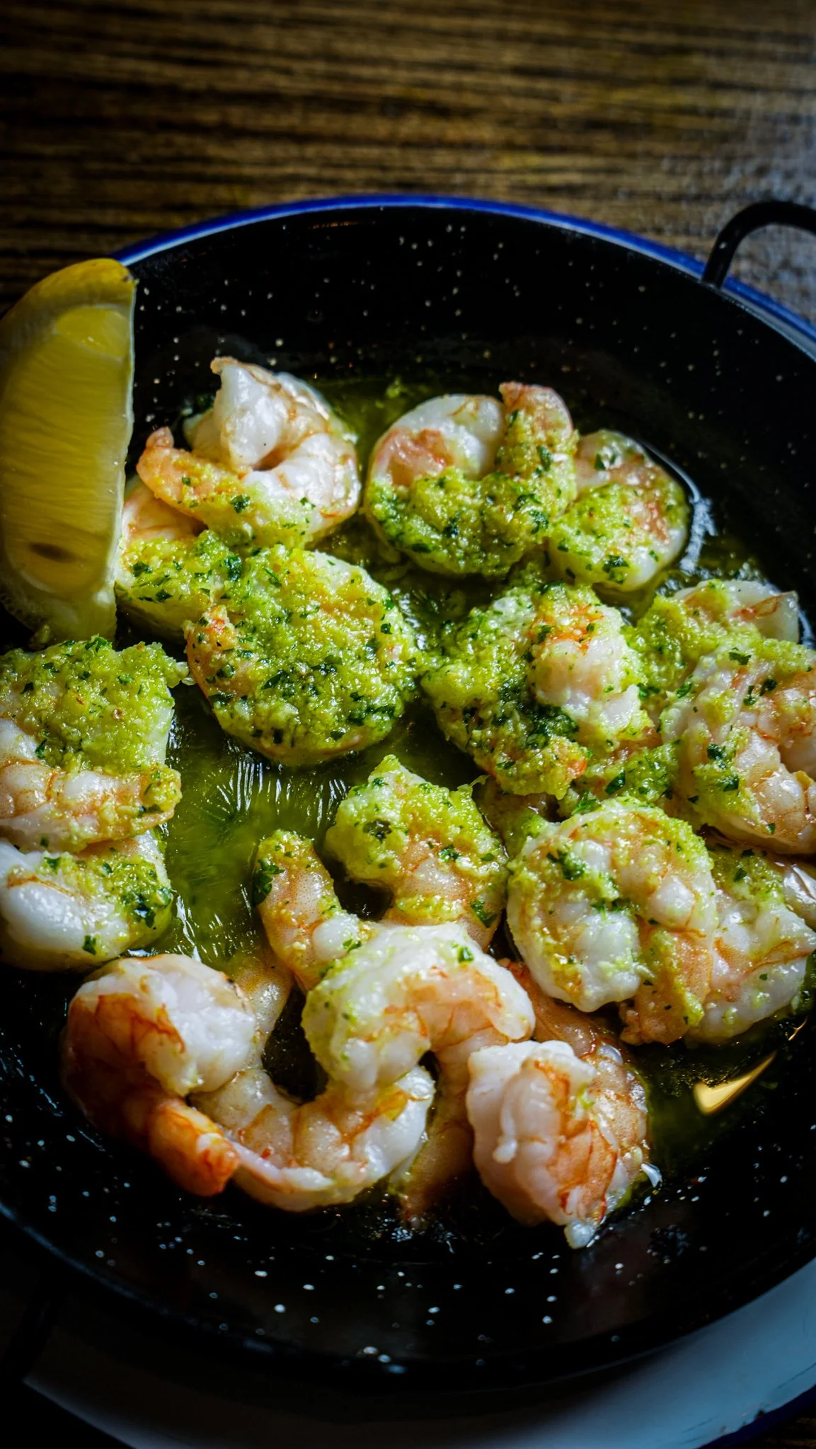 Shrimp in garlic butter sauce with parsley and lemon wedge in a black skillet.