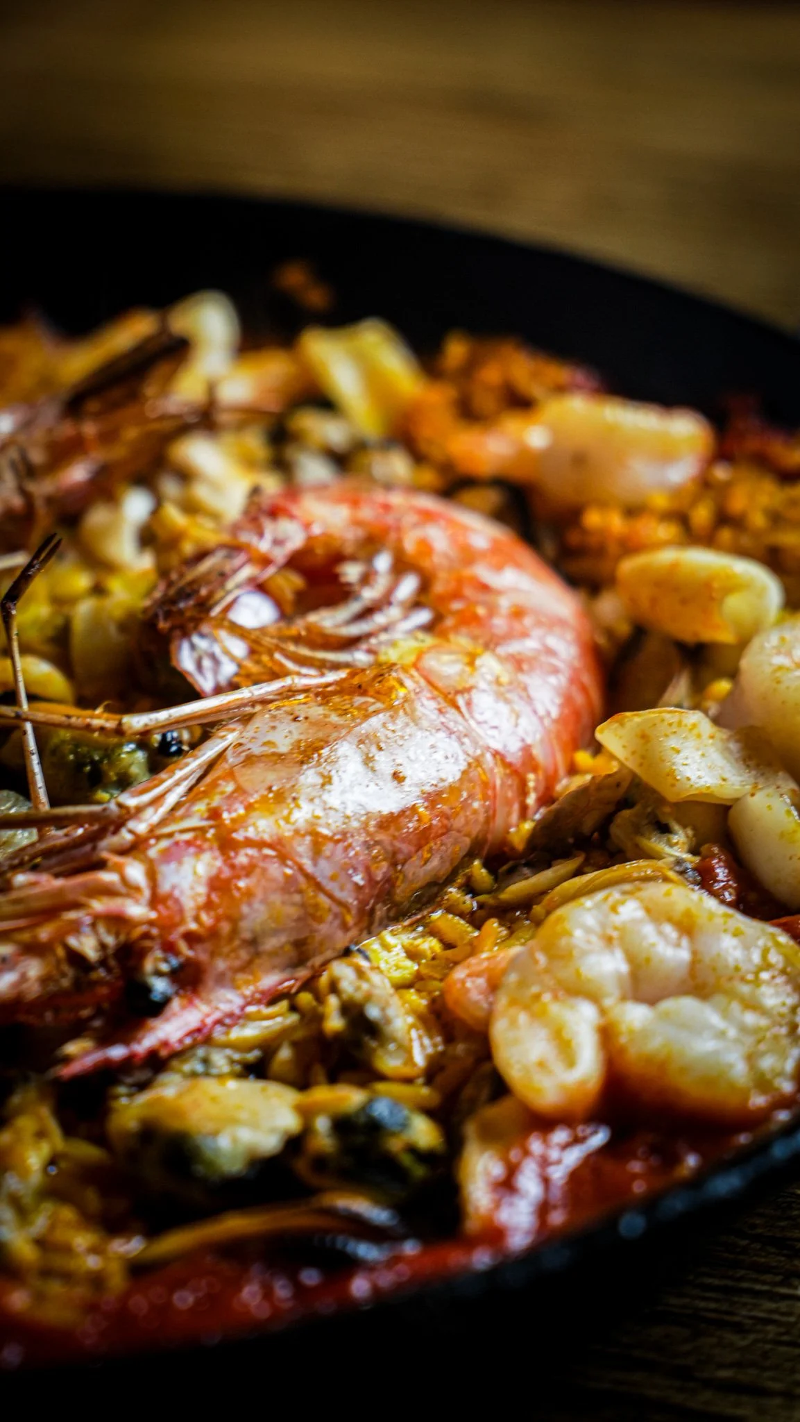 Close-up of cooked seafood in a black pan, featuring a large shrimp, chopped garlic, and other seafood ingredients.