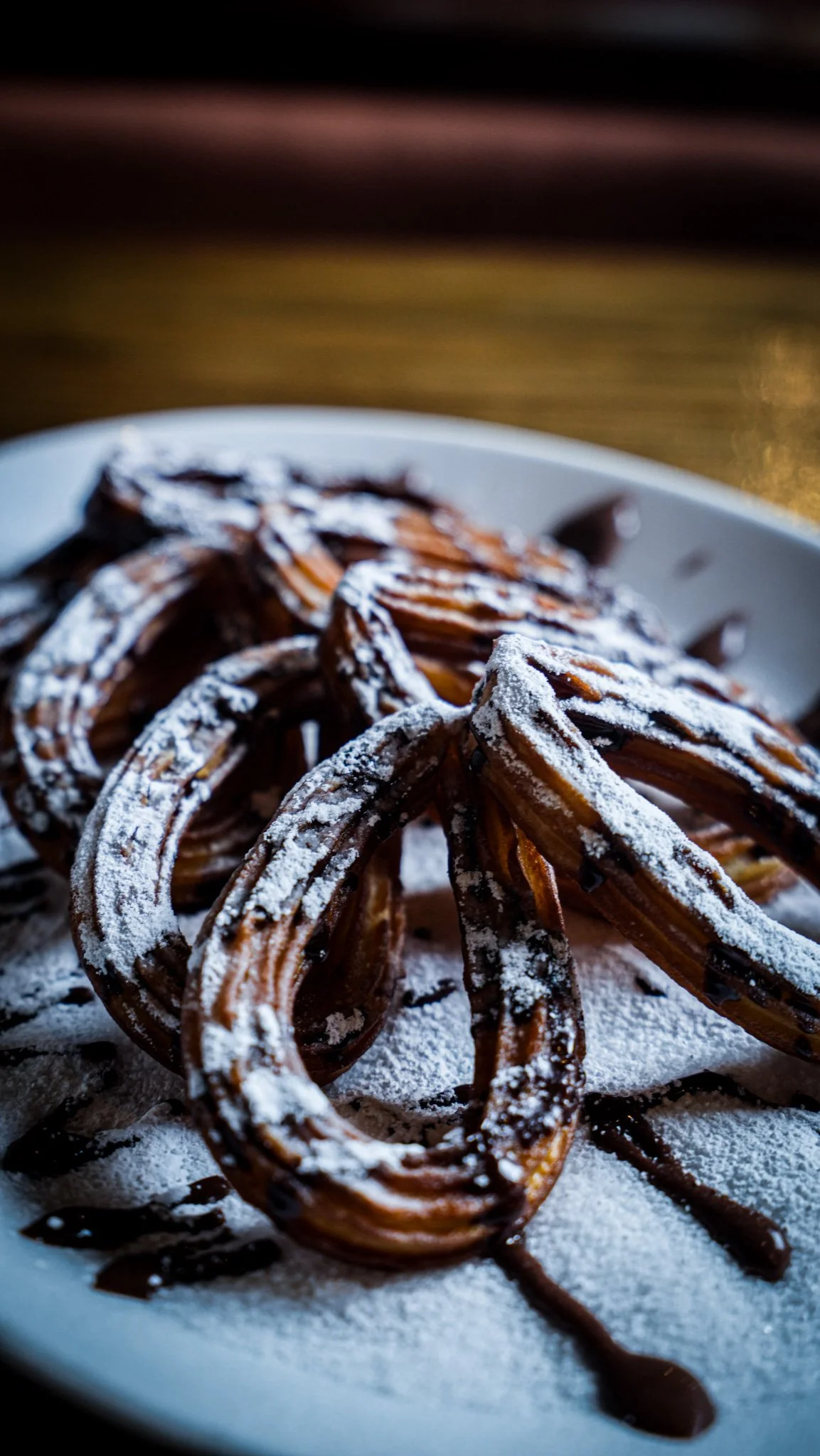 Churros dusted with powdered sugar on a plate with chocolate drizzle