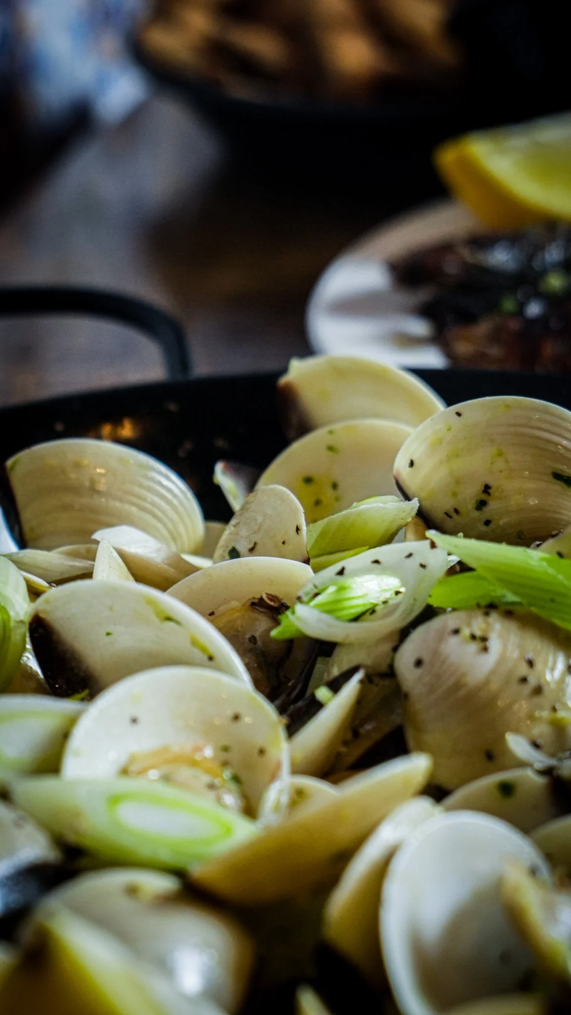 Close-up of cooked clam shells with green onion and herbs in a black skillet.