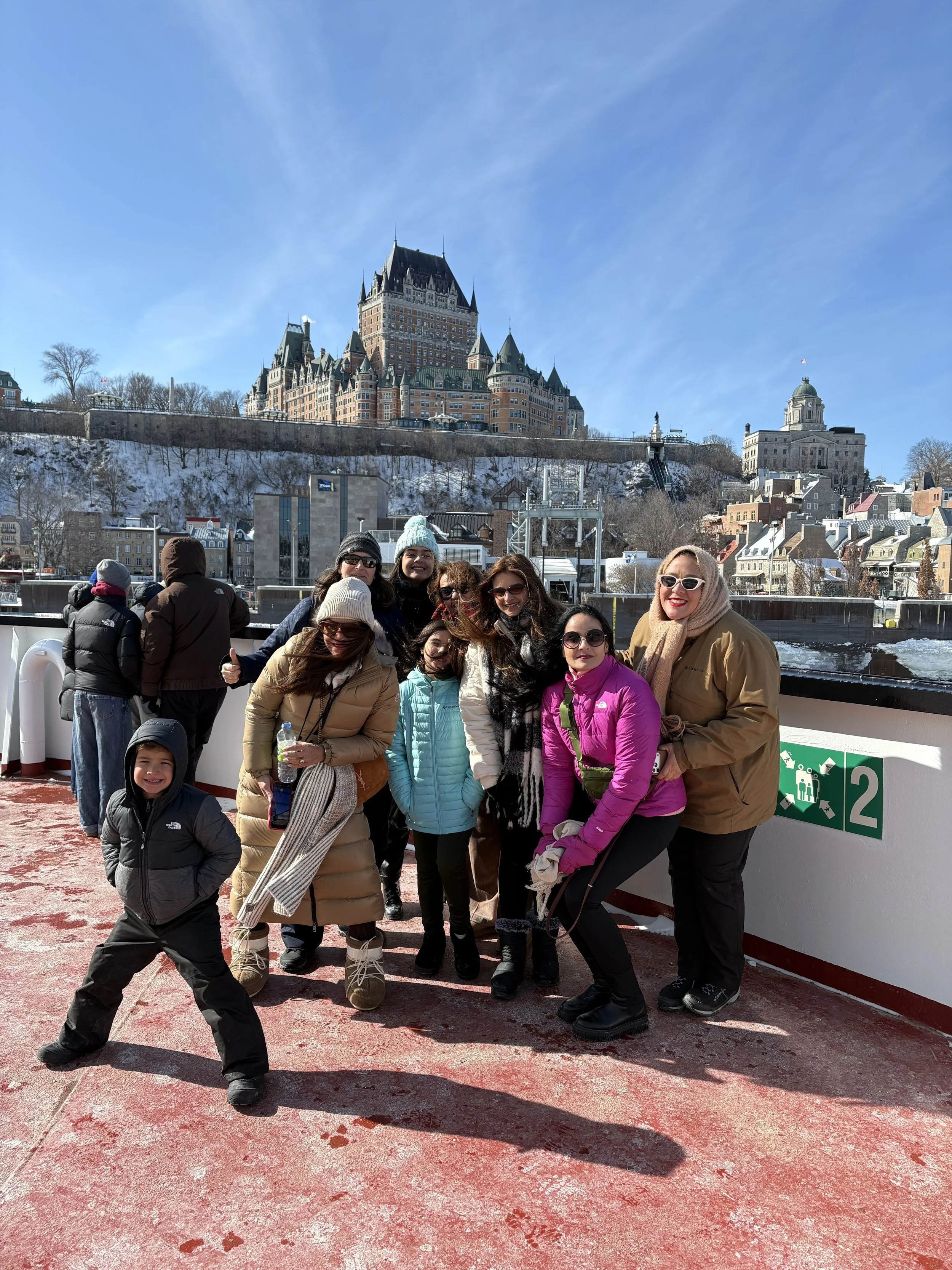 Group of smiling people on a boat with a snowy castle in the background, on a bright winter day.