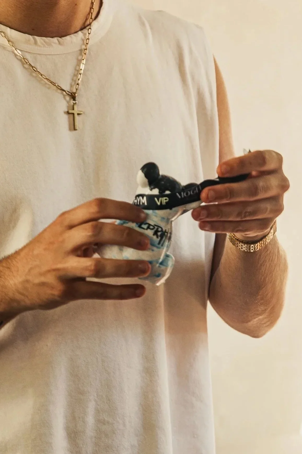 Person wearing a white sleeveless shirt and gold jewelry holding a small ice cream container and a black spoon.