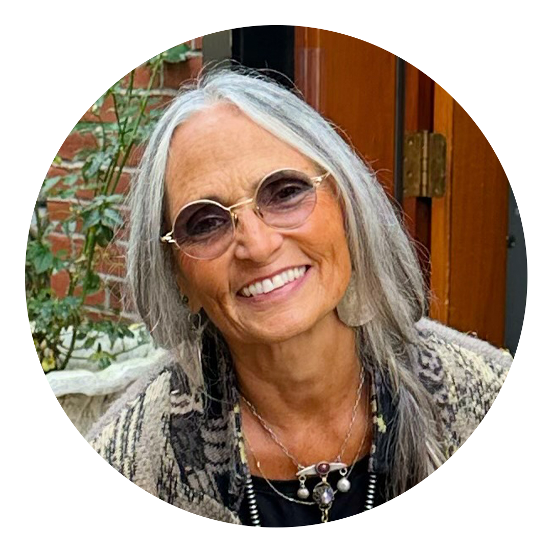 Image of Melinda Salazar, a Latina/Ukrainian woman with straight grey-white hair smiling with circular glasses and handmade jewelry