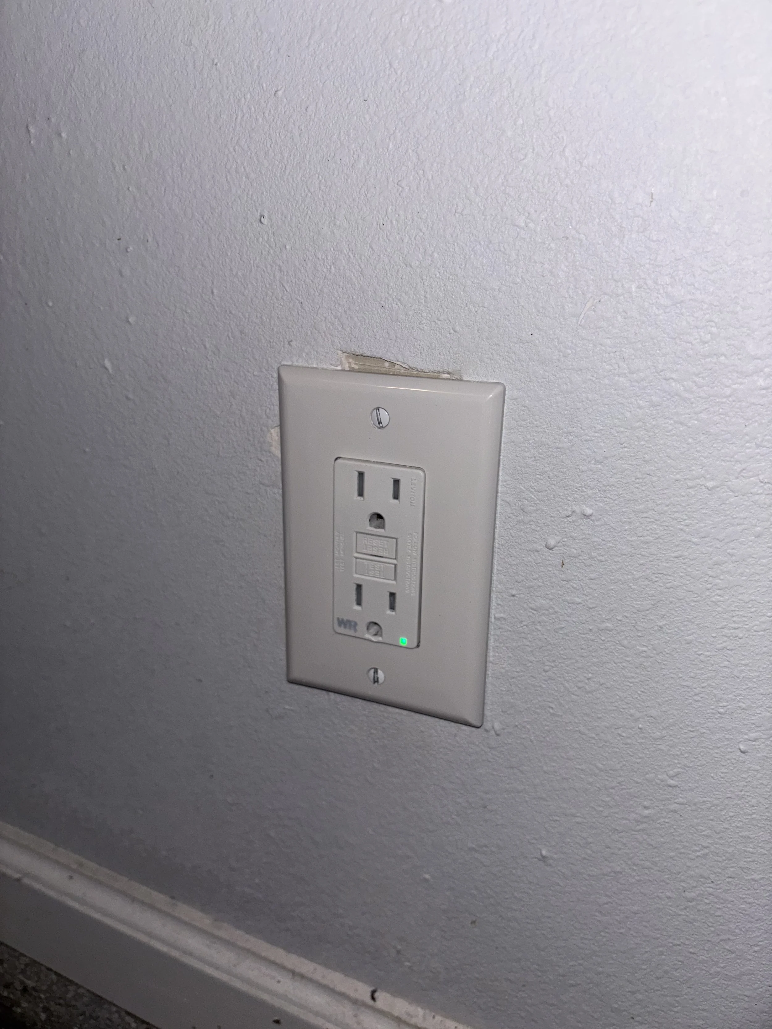 Electrical outlet with a green indicator light on a textured white wall.
