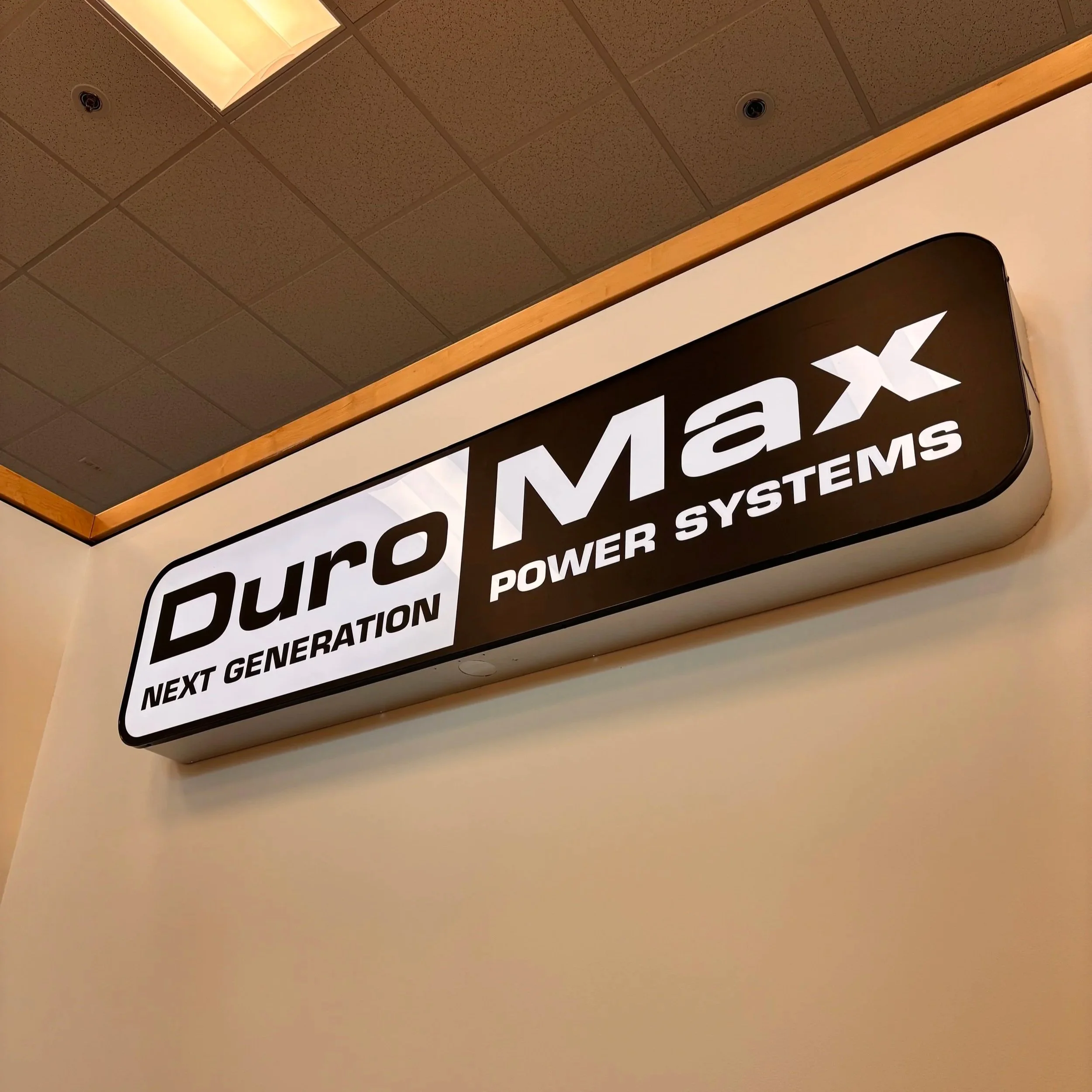 Illuminated sign for DuroMax Power Systems, with the words "Next Generation" below the brand name, mounted on a wall near the ceiling.