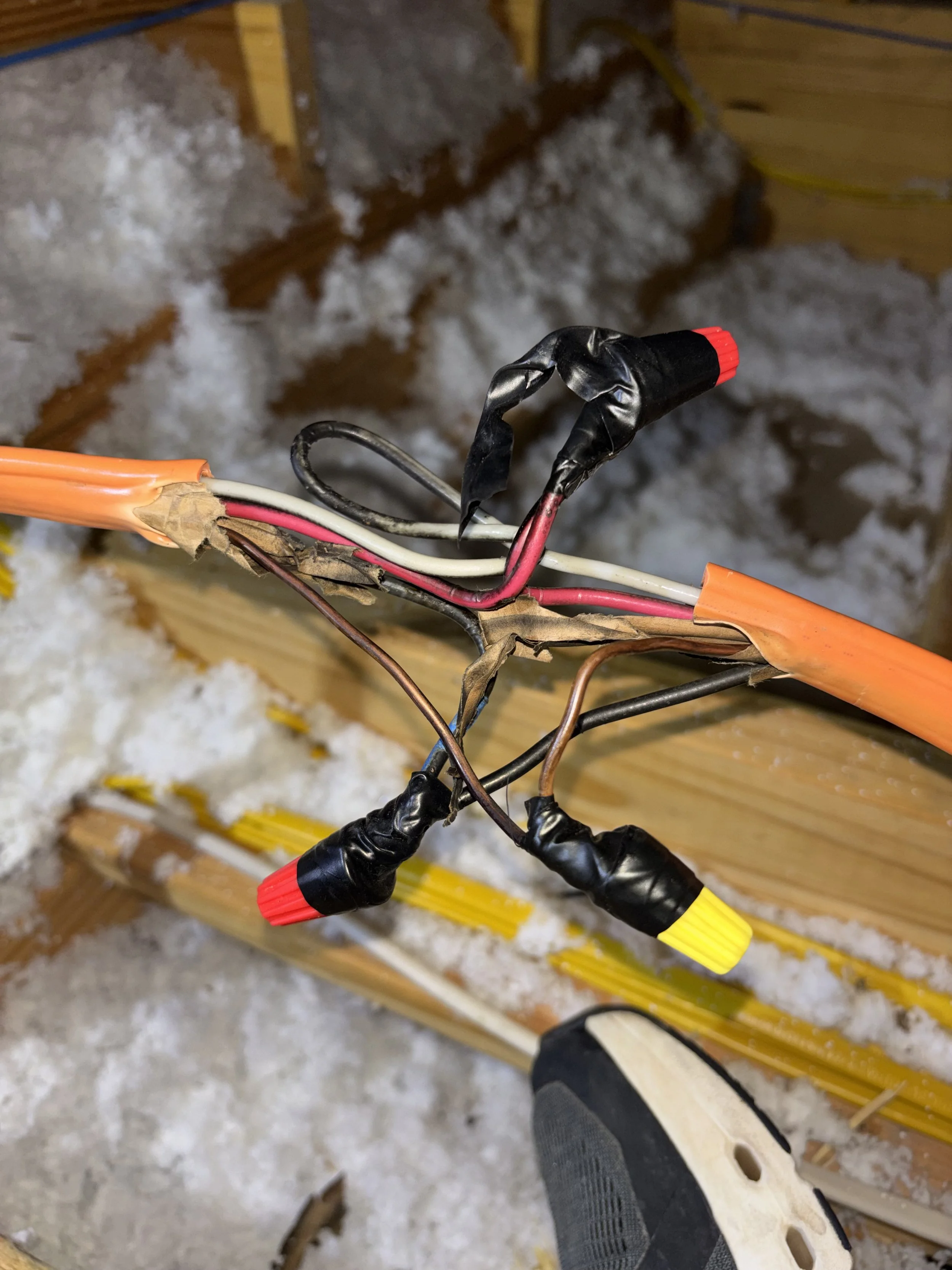 Exposed and damaged electrical wires with electrical tape, with a snowy background and part of a shoe visible.