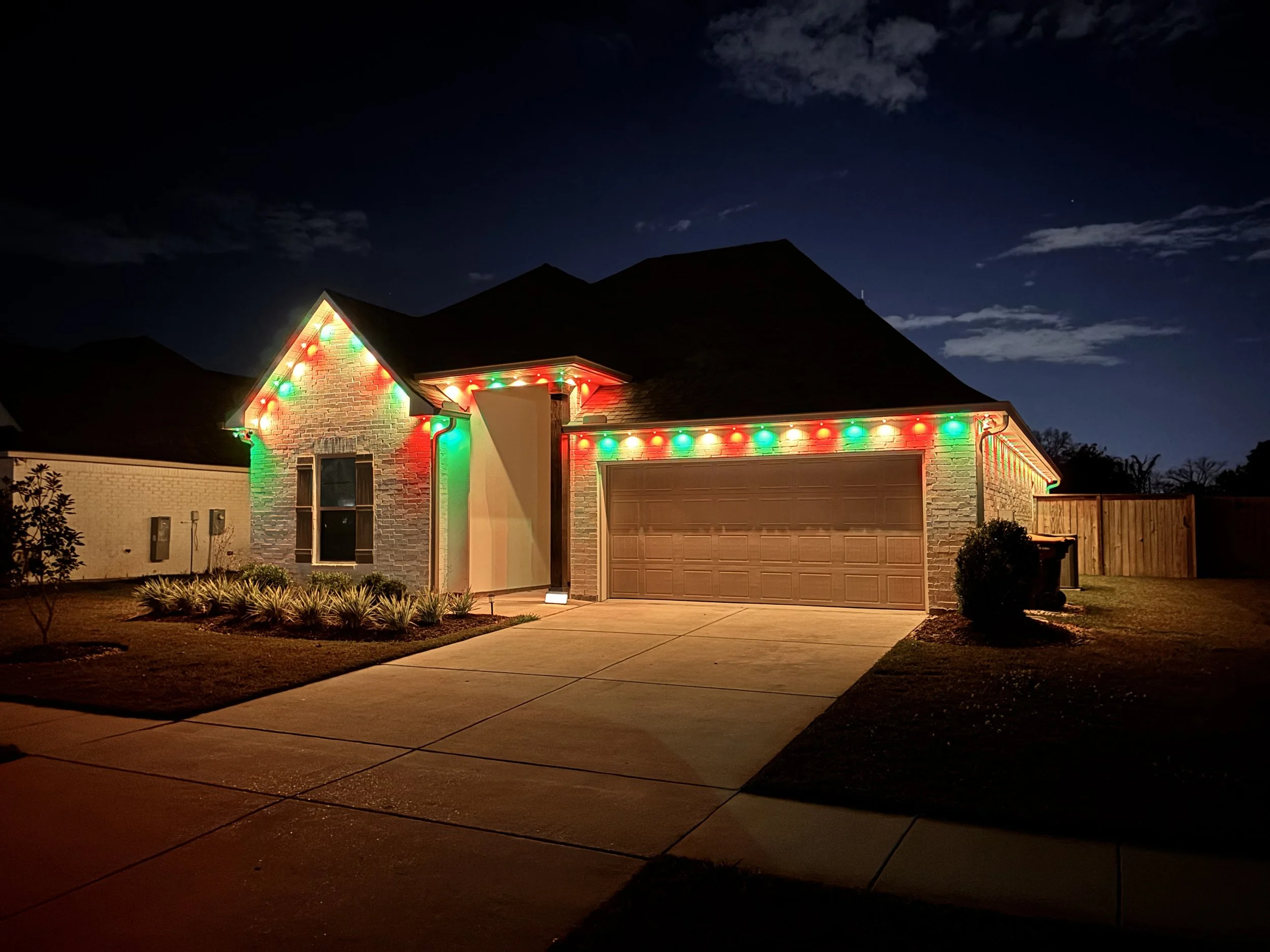 House decorated with multicolored Christmas lights at night, with a dark sky and few clouds.