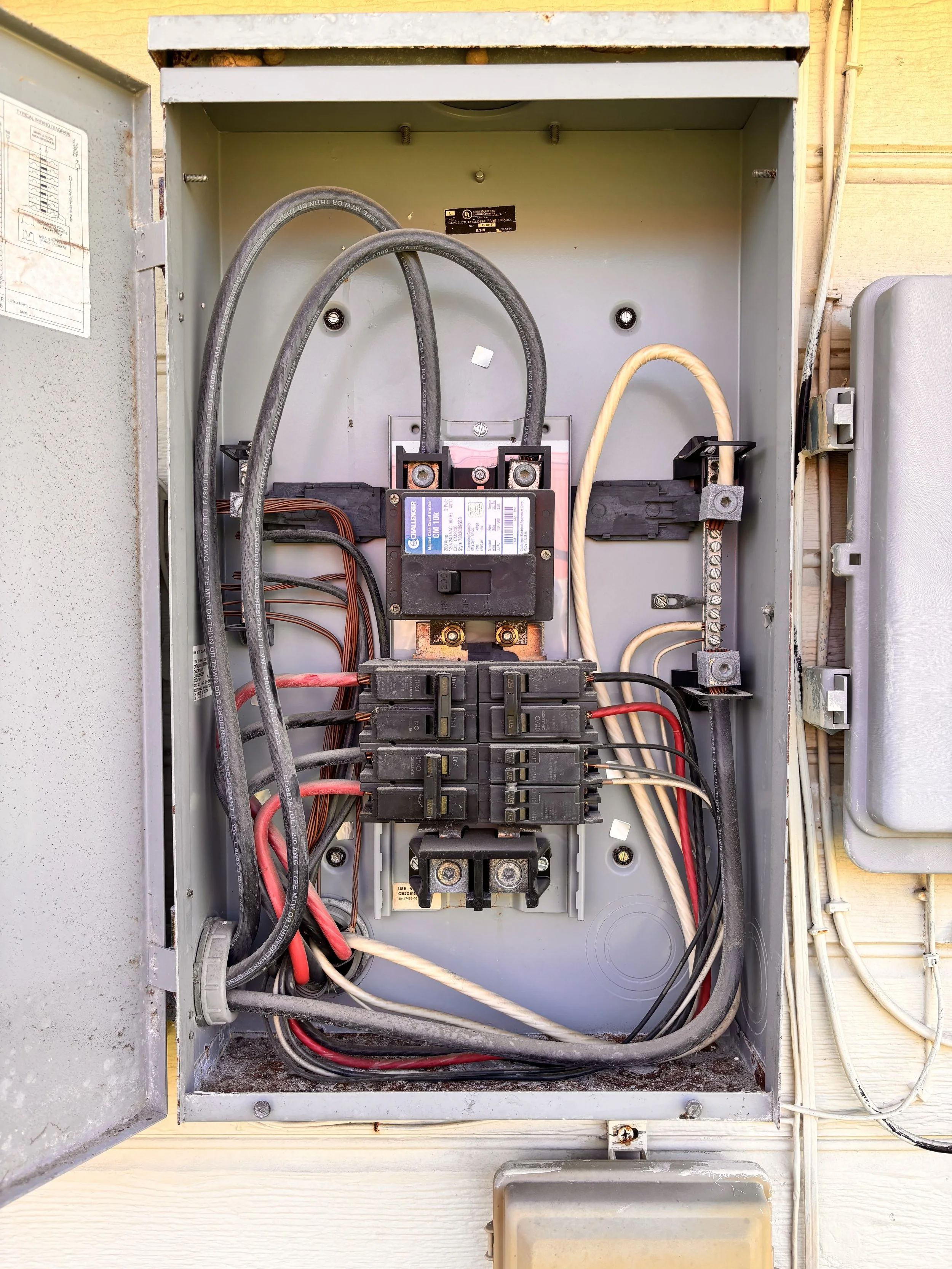 Open electrical meter box with circuit breaker panel inside, showing various wires connected to the breakers.