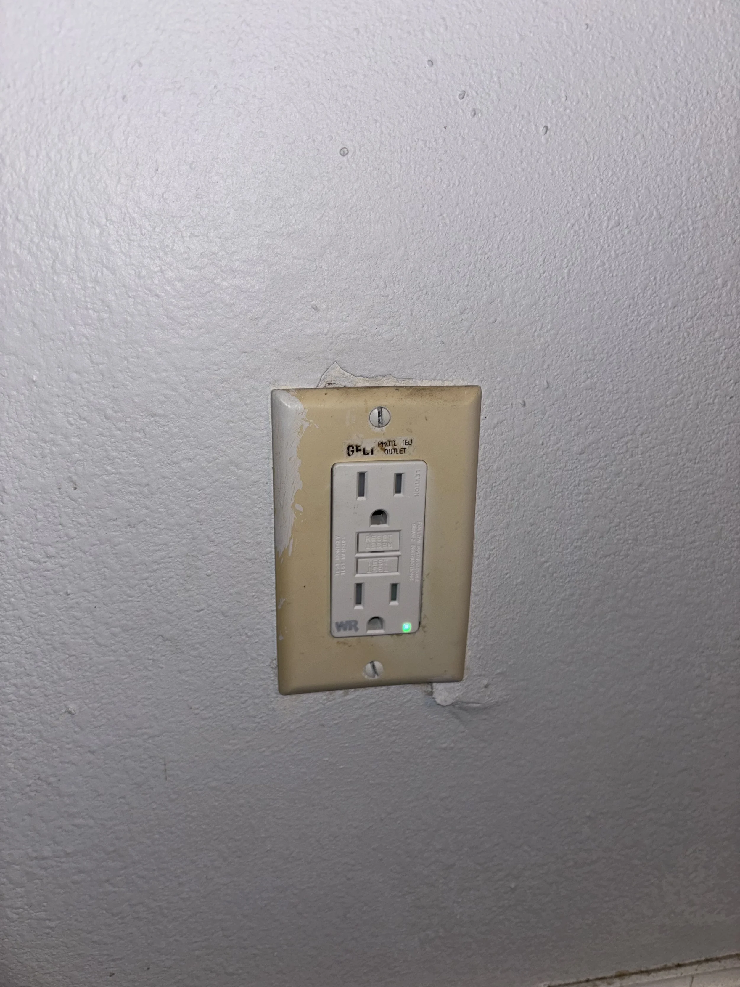 Electrical outlet on a textured ceiling with a green light indicating power.