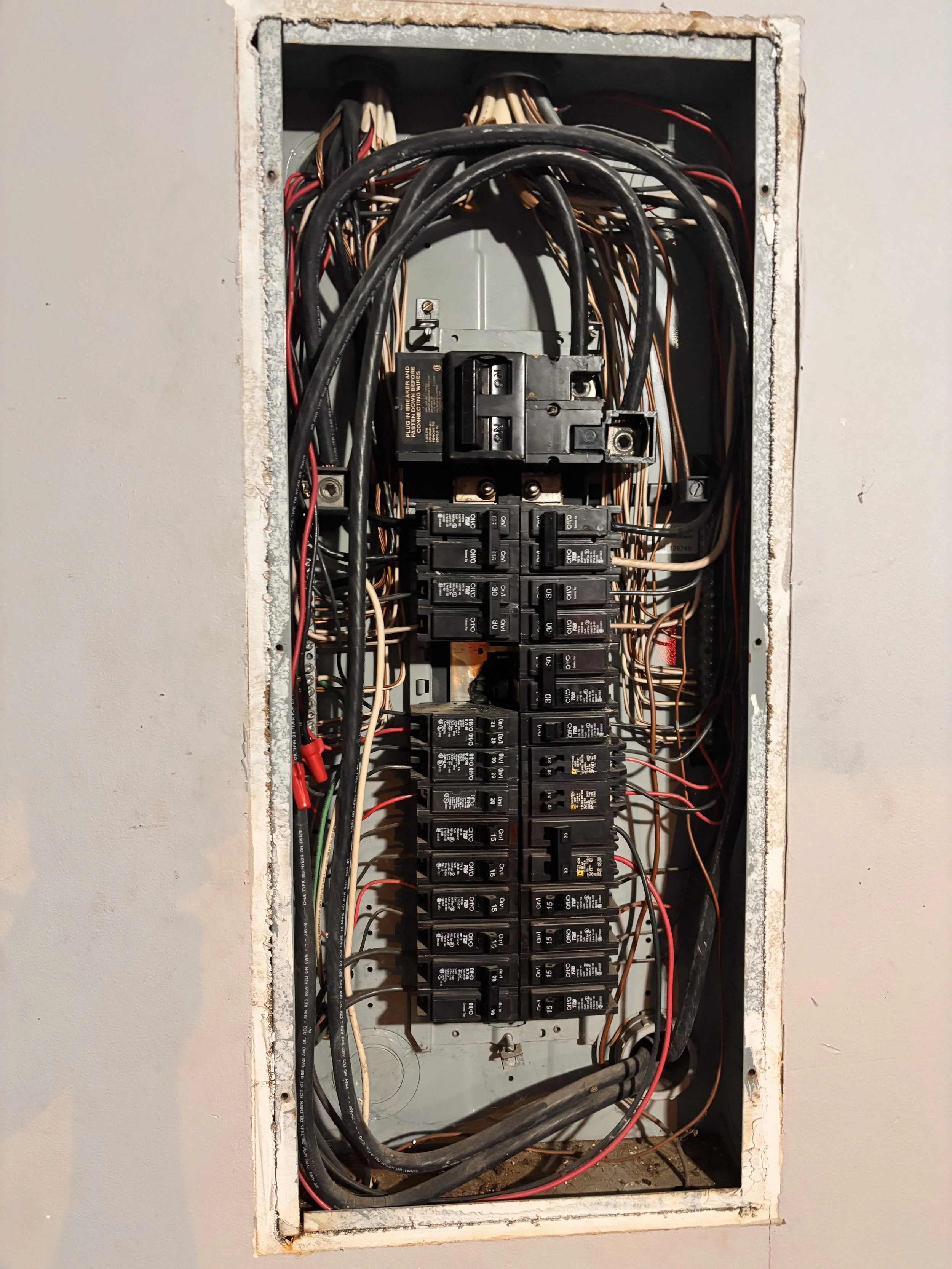 Close-up of an electrical breaker panel with multiple circuit breakers and wiring inside an unfinished wall.
