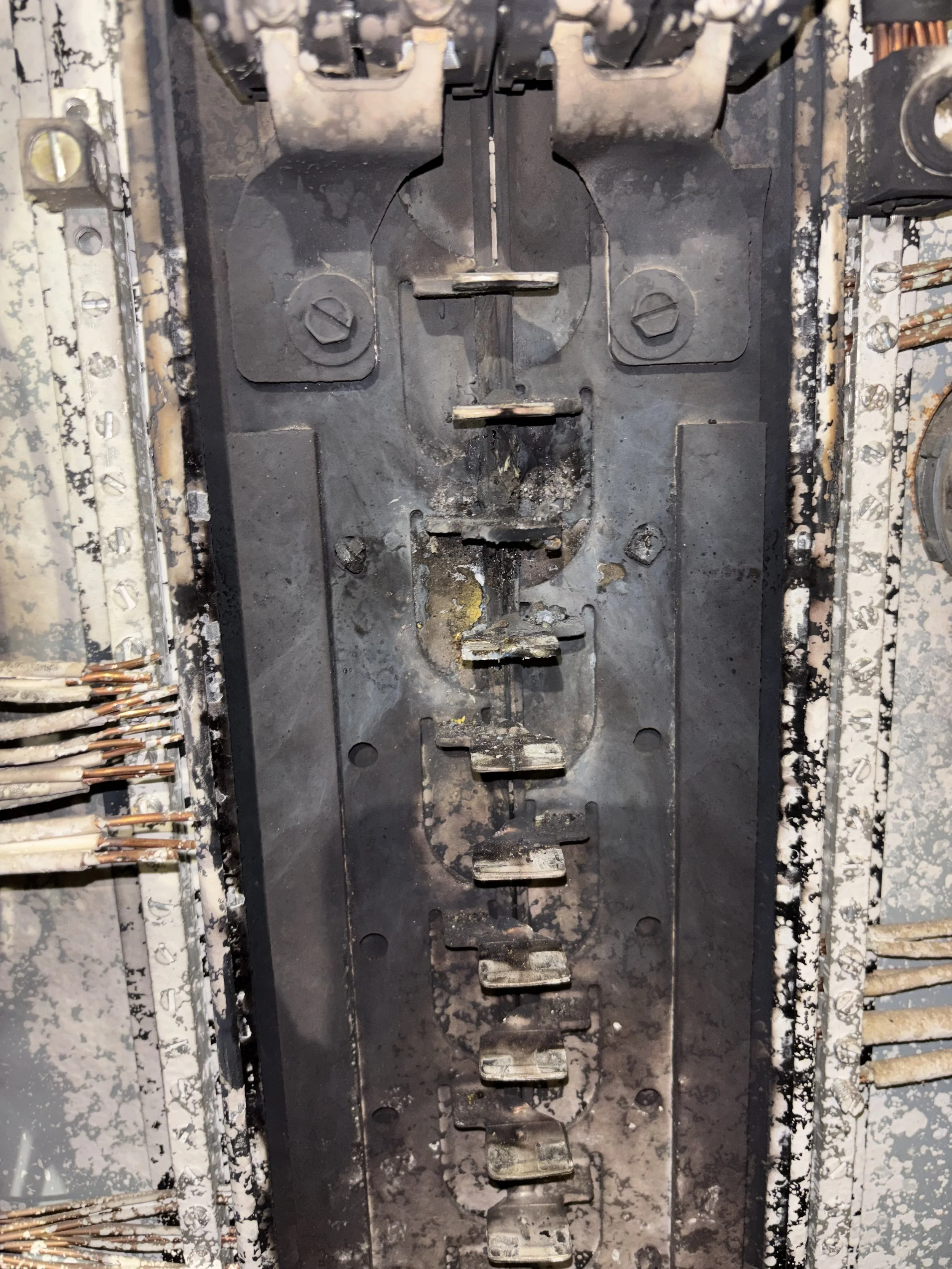 Close-up view of an electrical breaker panel with broken and burnt circuit breakers and wires.