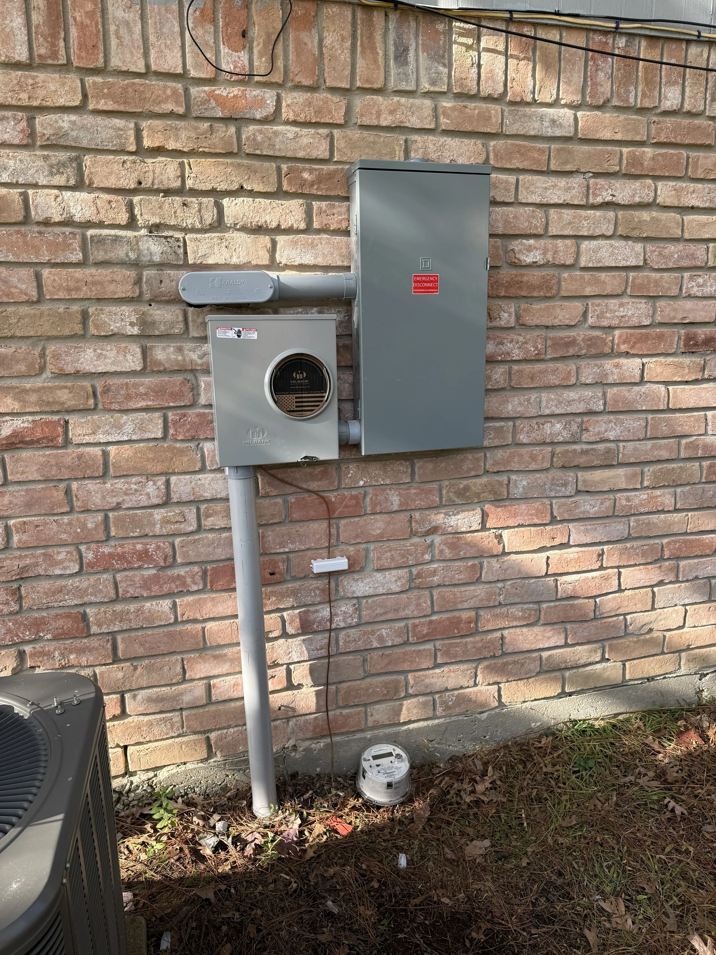 Outdoor electrical meter and breaker box mounted on brick wall.