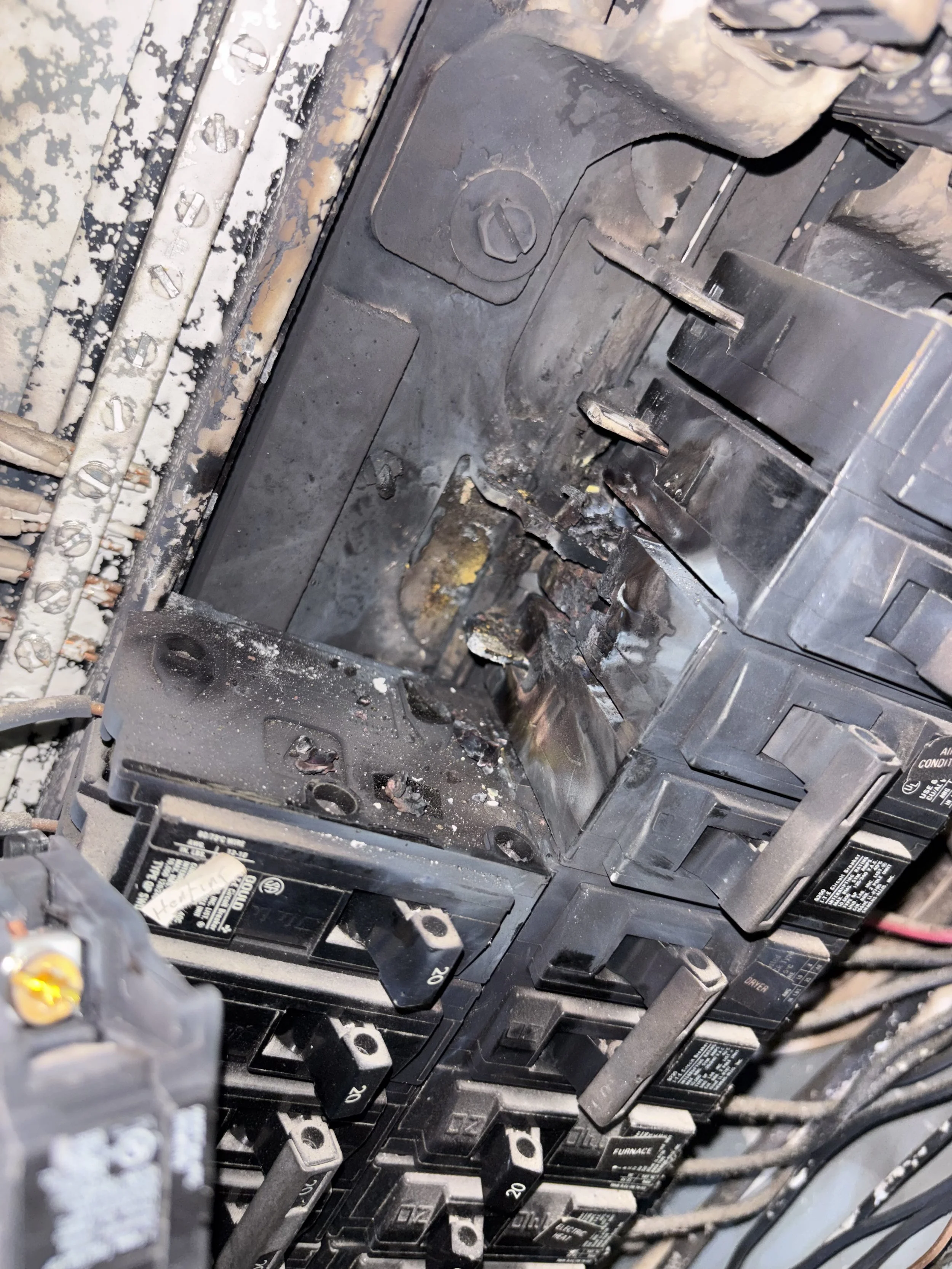 An electrical panel shows signs of fire damage with burnt components and soot.