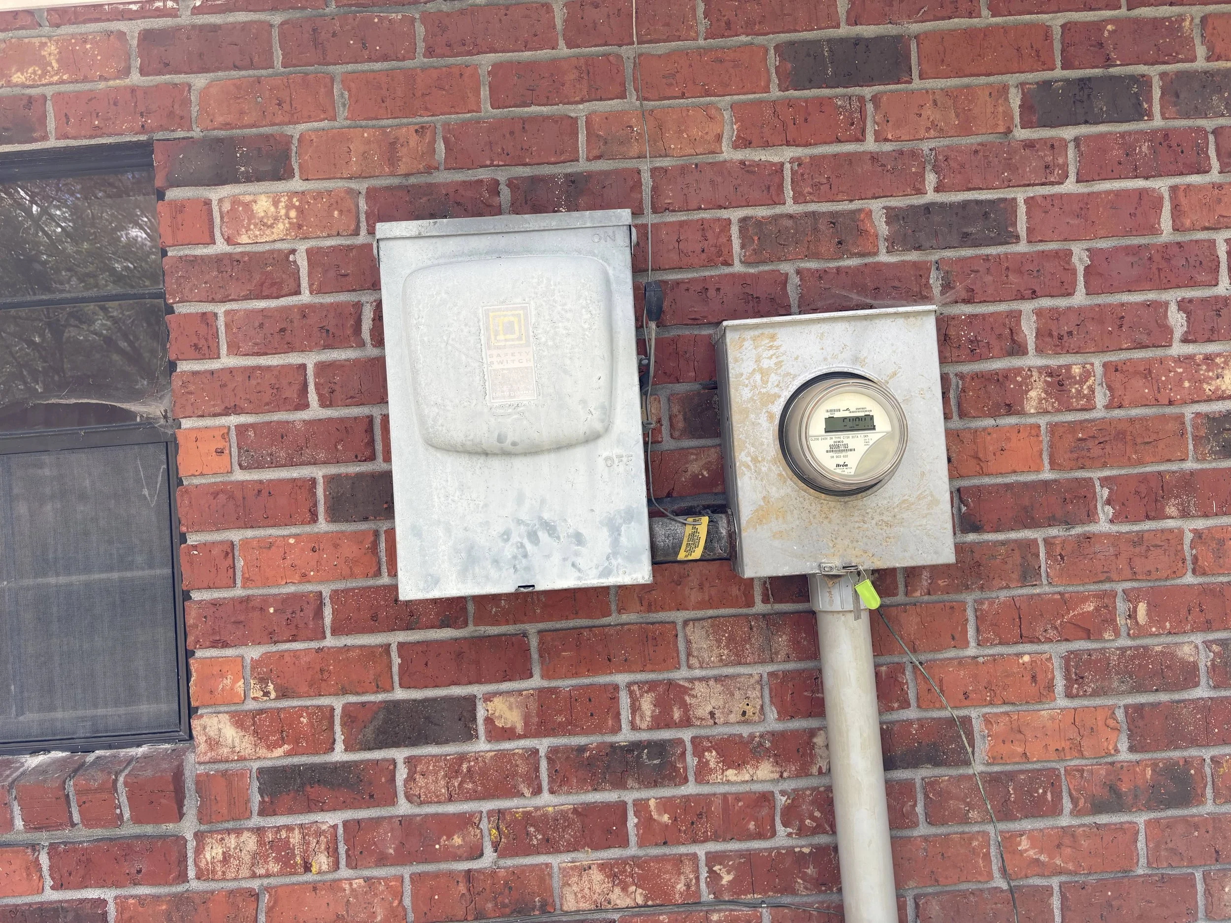 Electric meter and circuit box mounted on red brick wall outside a building.