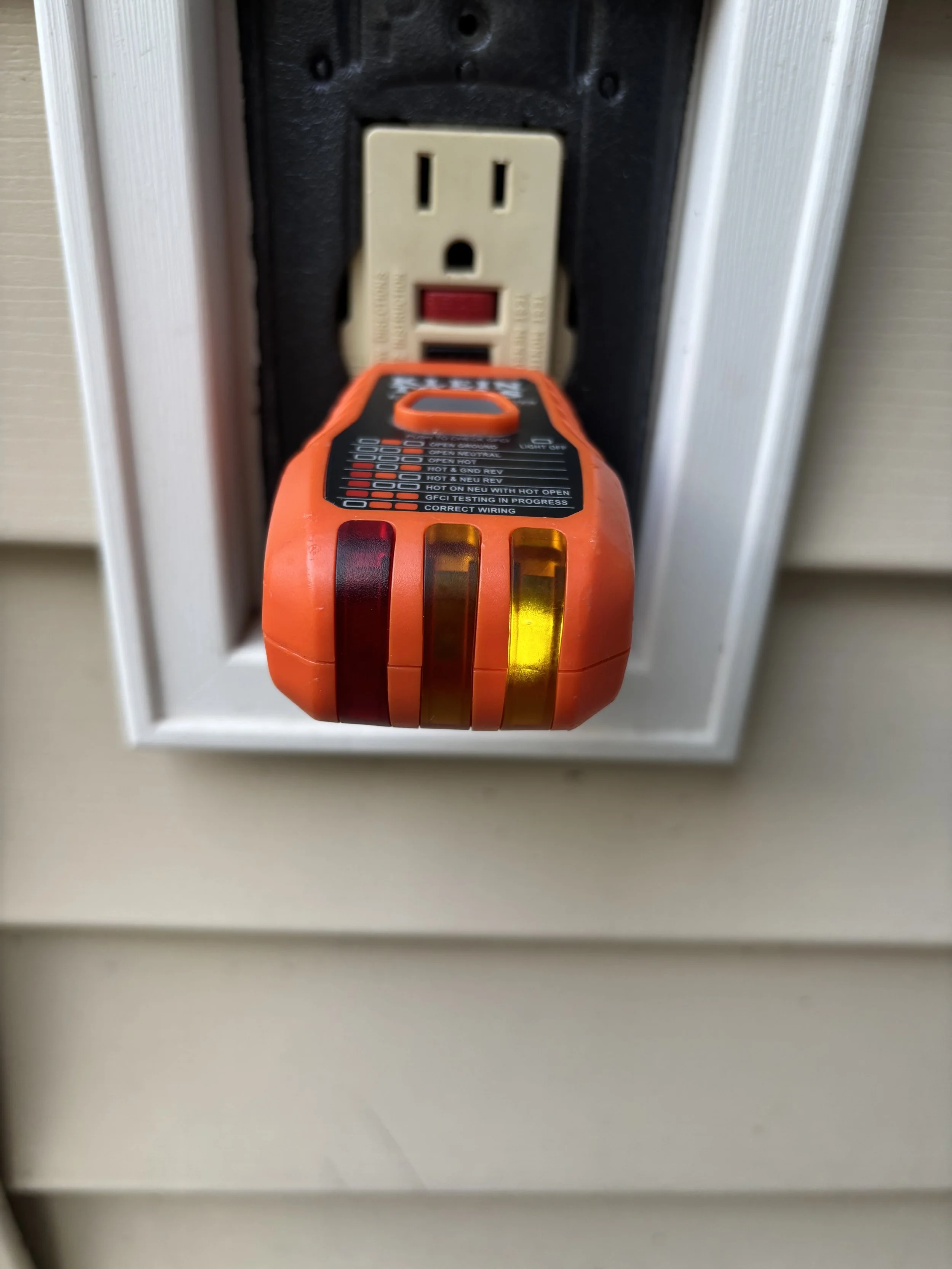 A circuit tester hanging in front of an electrical outlet.