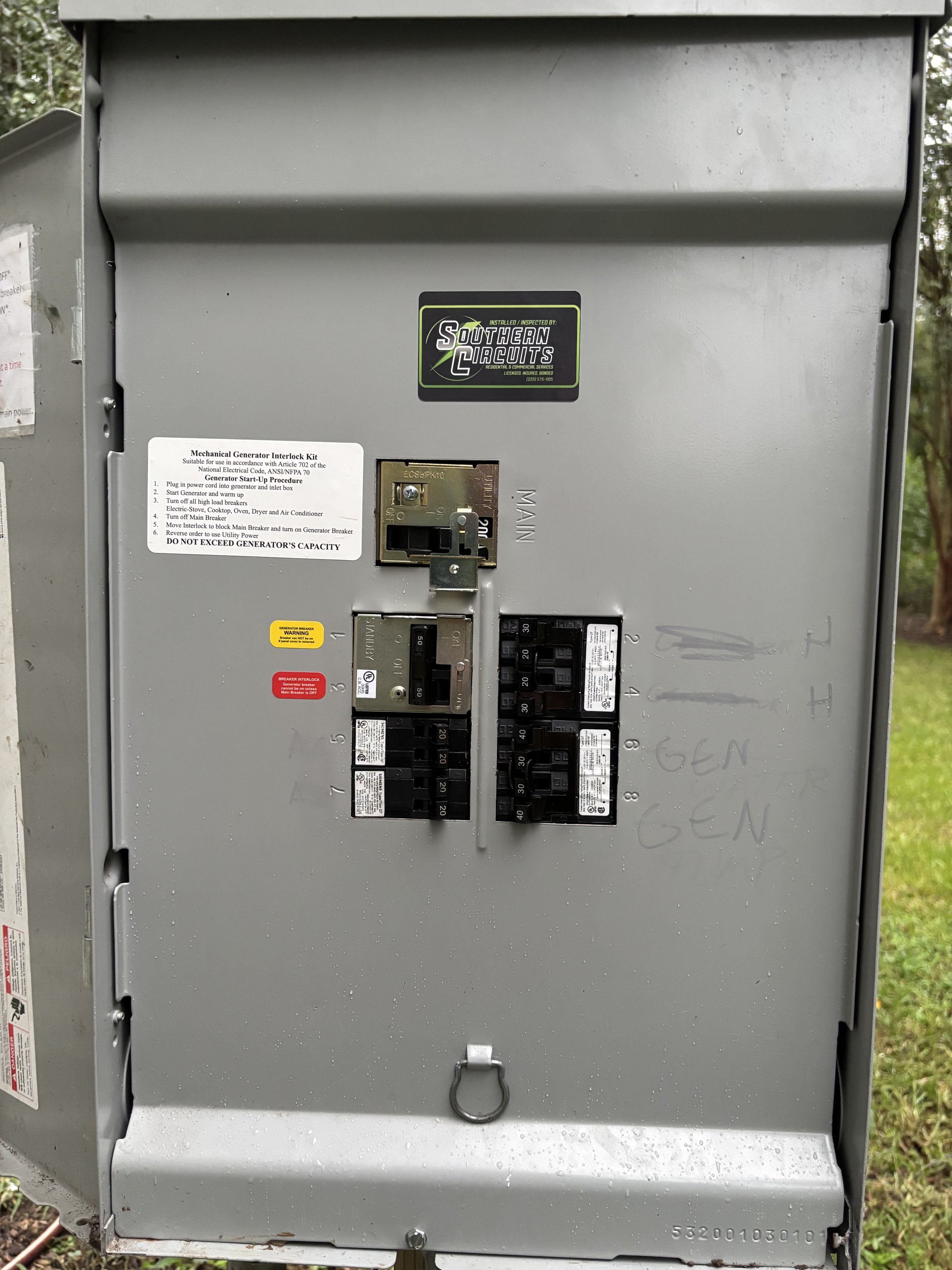 An electrical panel with circuit breakers and labels, mounted outdoors, labeled with handwritten notes and regulatory stickers.
