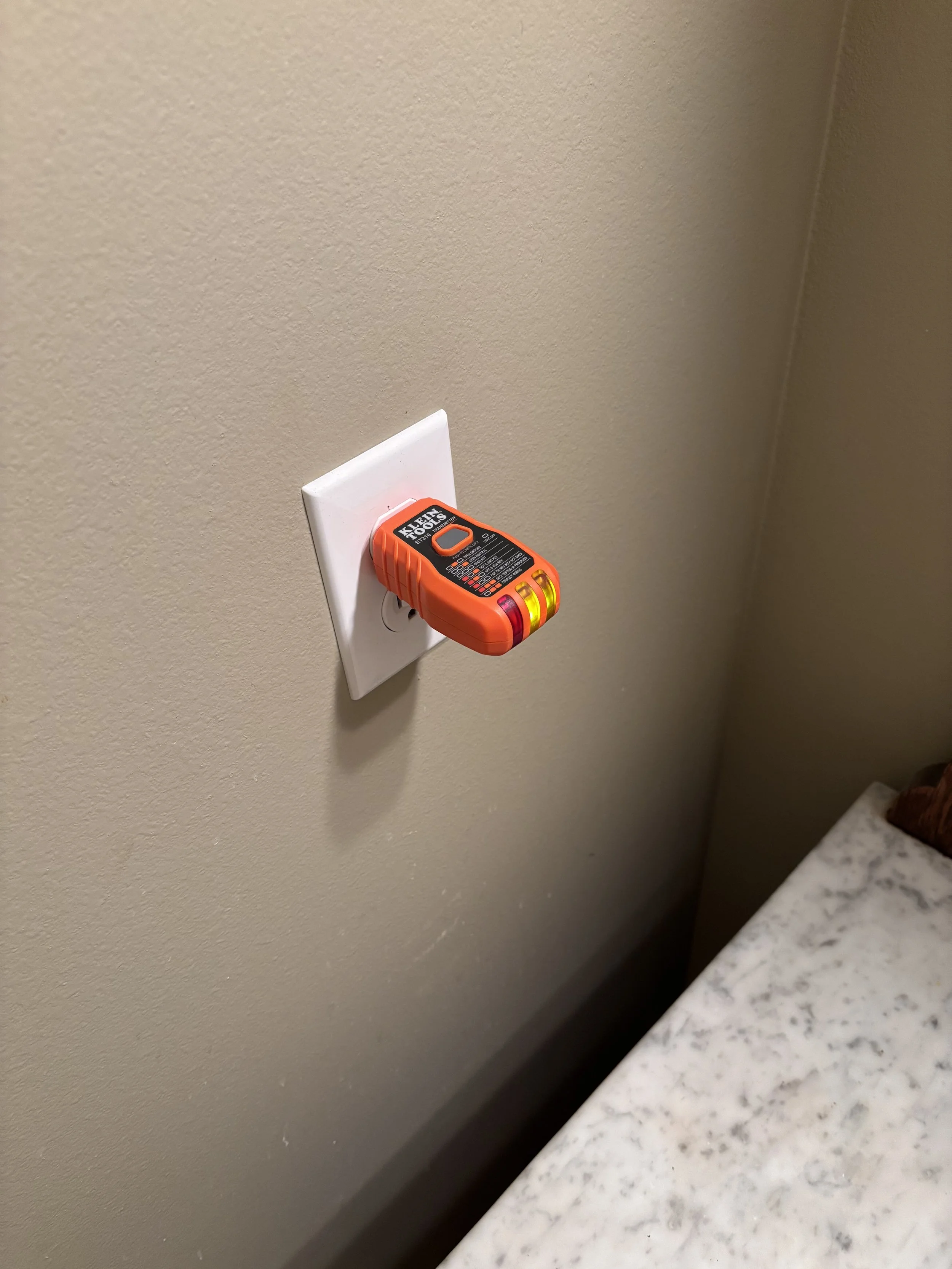A bright orange real estate agent lockbox attached to a white electrical outlet on a beige wall.