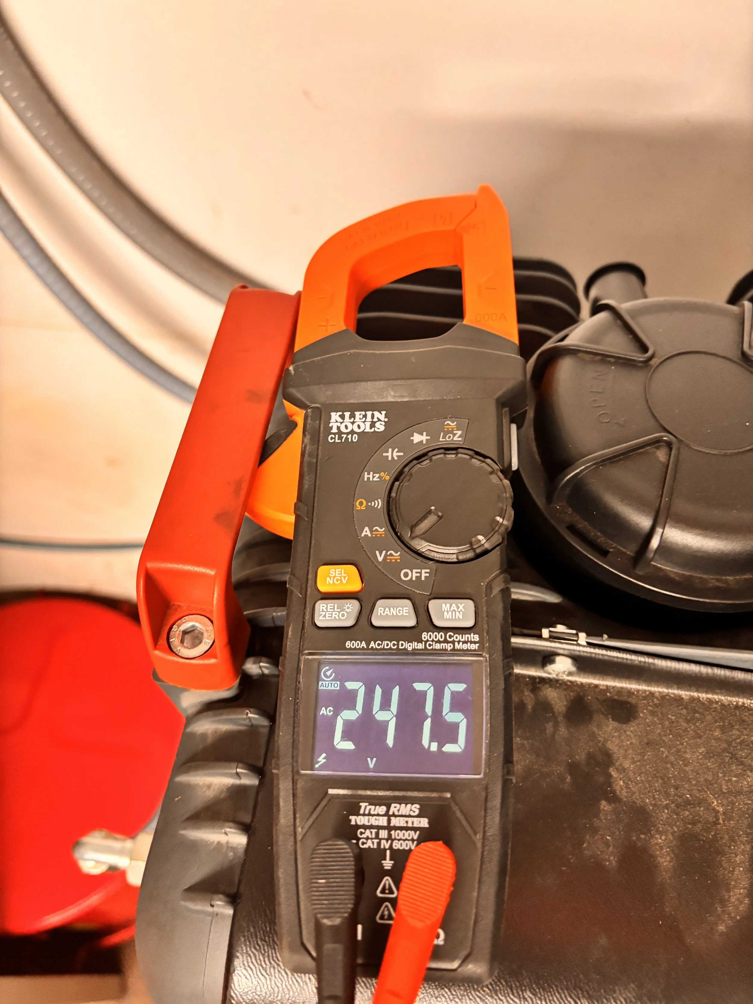Digital clamp meter measuring 247.5 volts AC connected to a power source.