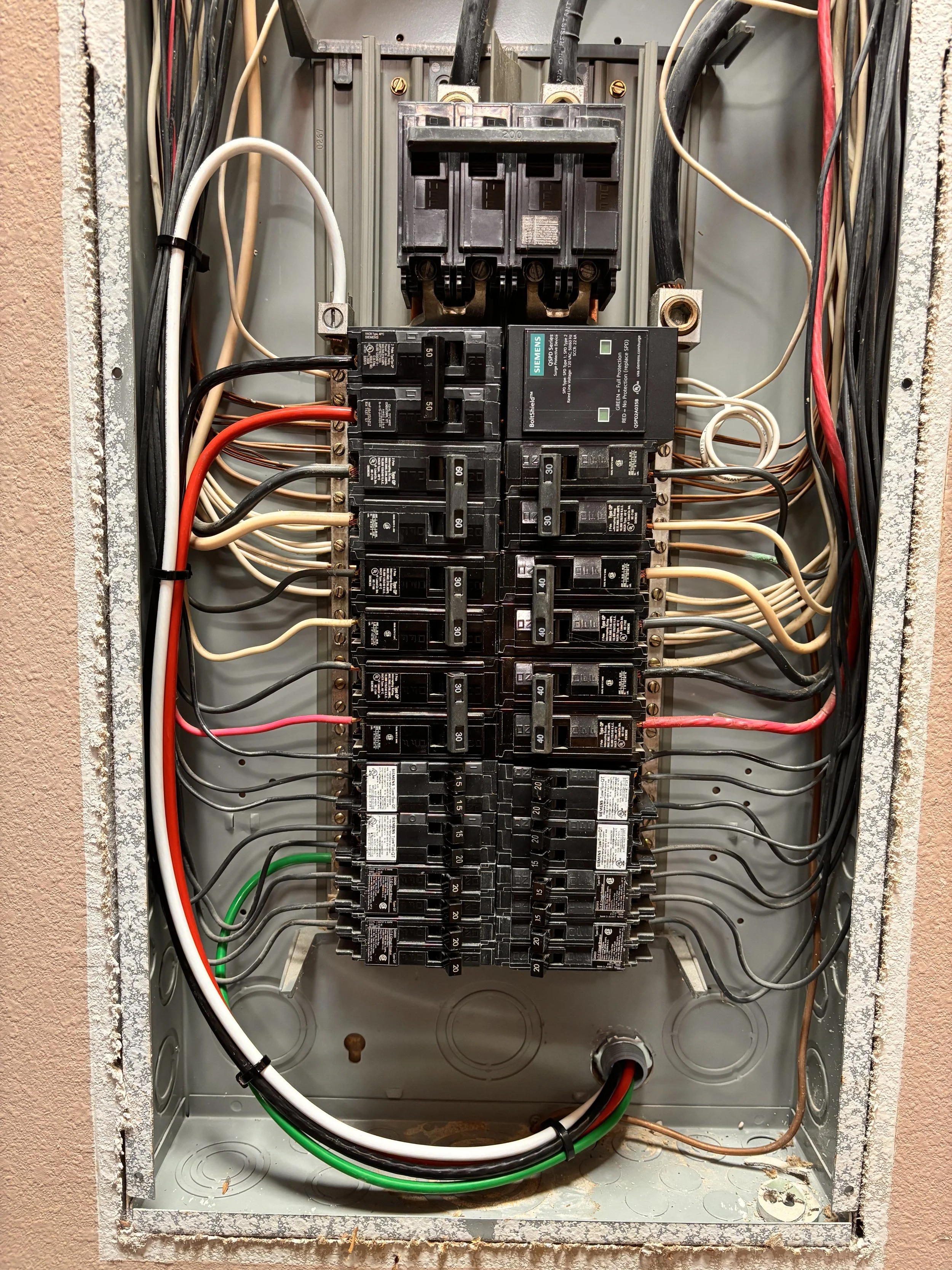 An electrical panel with multiple black circuit breakers and some colored wires inside a metal box.