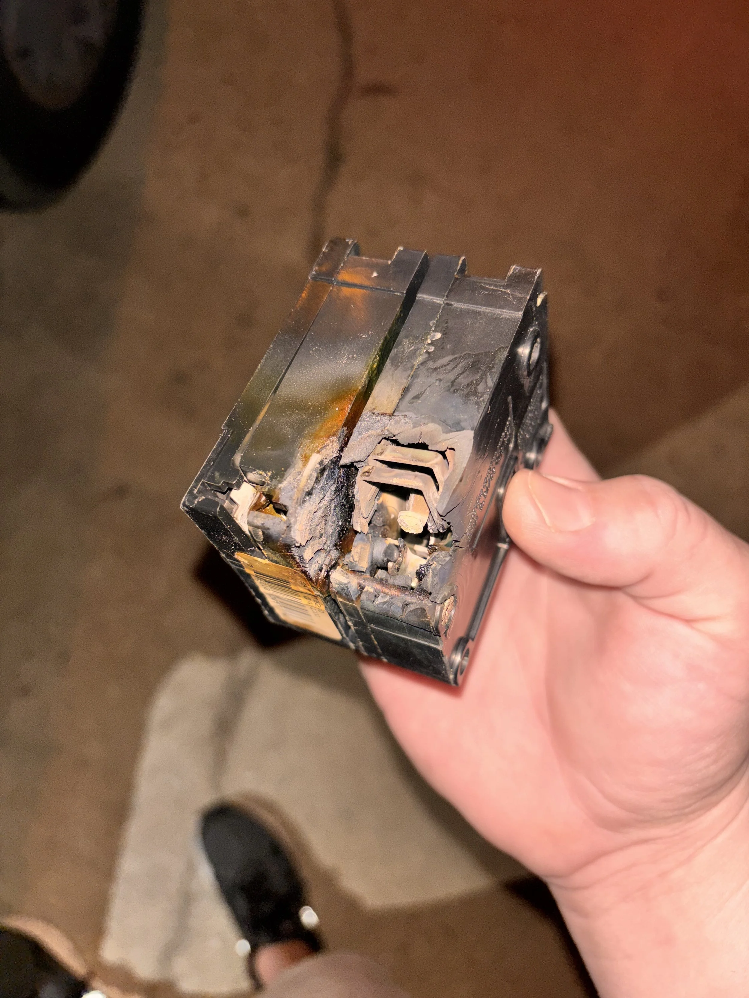 A person is holding a burnt and damaged electrical circuit breaker.